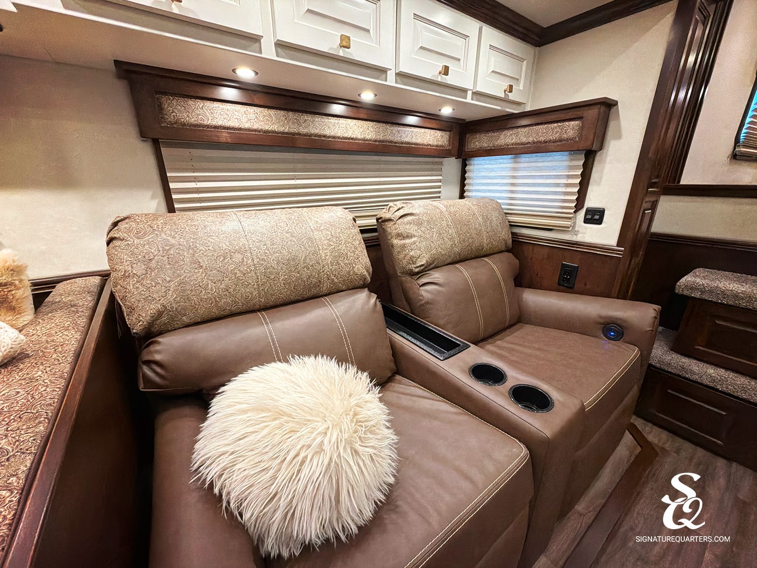 Interior view of a luxury RV living area with brown leather recliners, cupholders, and a center console.