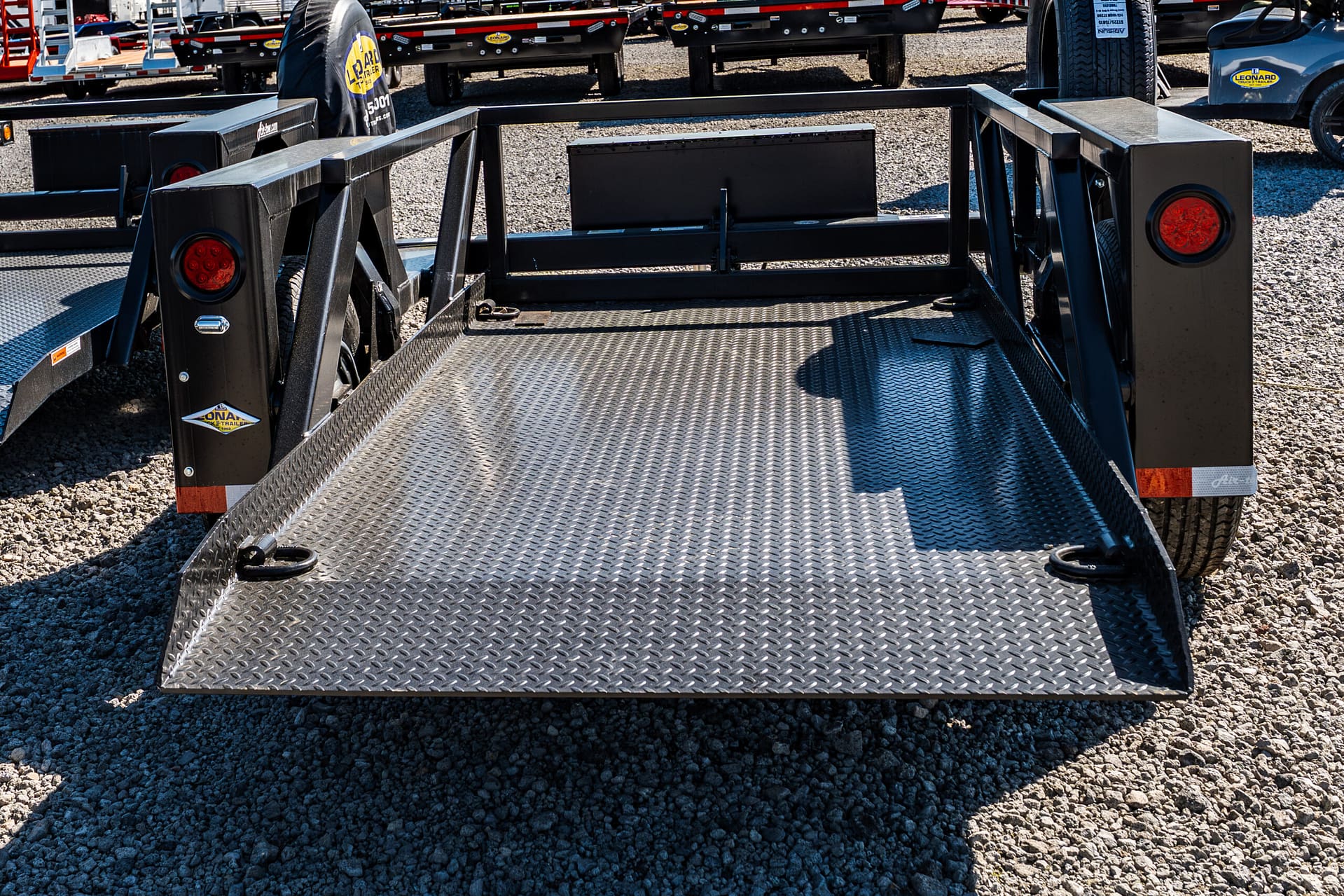 Diamond-plate flatbed trailer deck with side rails in a trailer yard; tires and other trailers visible in the background.