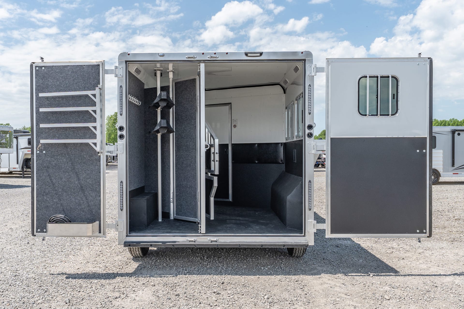 Open horse trailer at the rear with interior stalls, tack hooks, and an aisle (blue sky above).