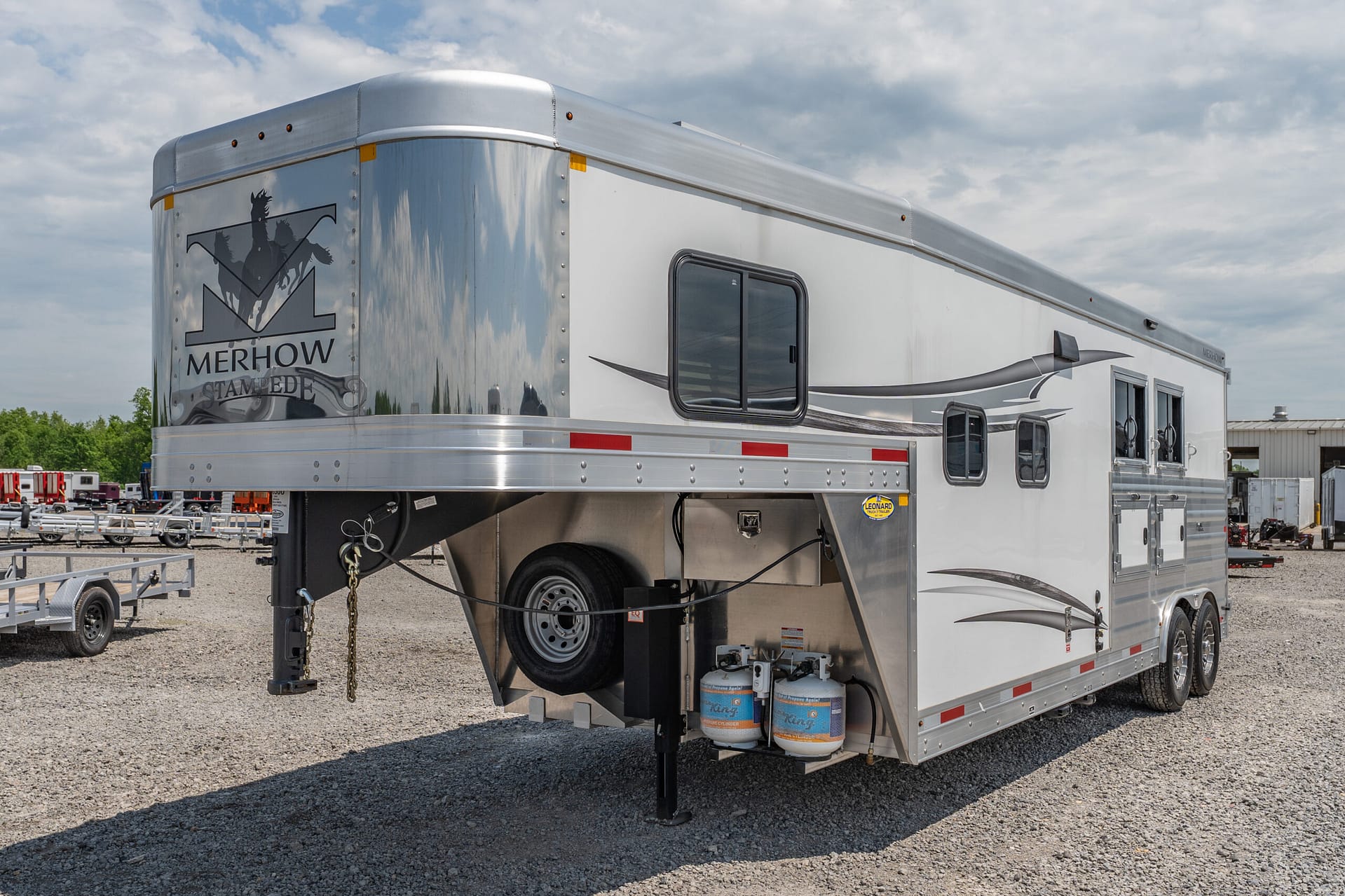 Silver Merhow Stampede horse trailer parked on gravel with logo on the rear panel and chrome trim