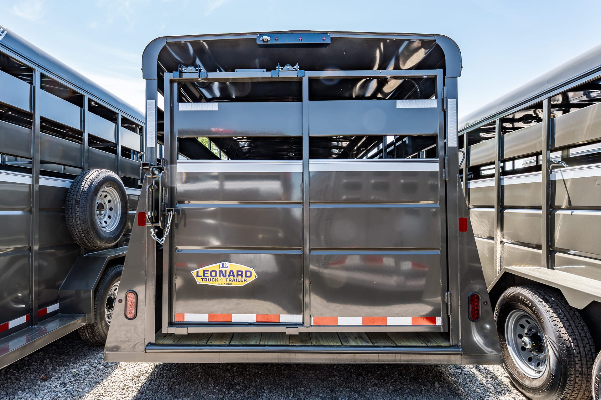 Rear loading ramp of a glossy gray livestock/trailer with an open gate and a Leonard Truck & Trailer logo on the back.