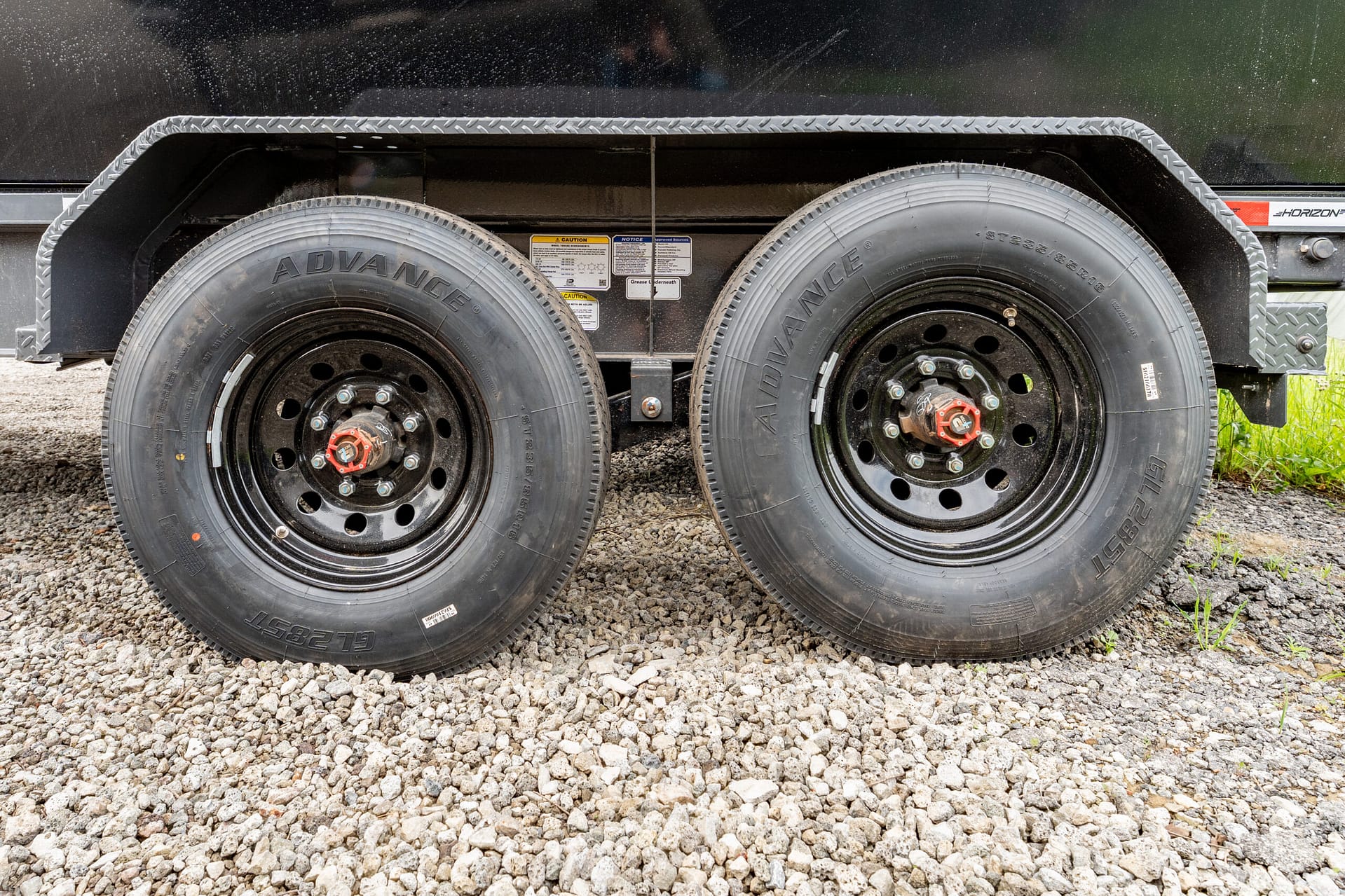 Dual wheels of a heavy-duty trailer with diamond-plate fender over a gravel surface