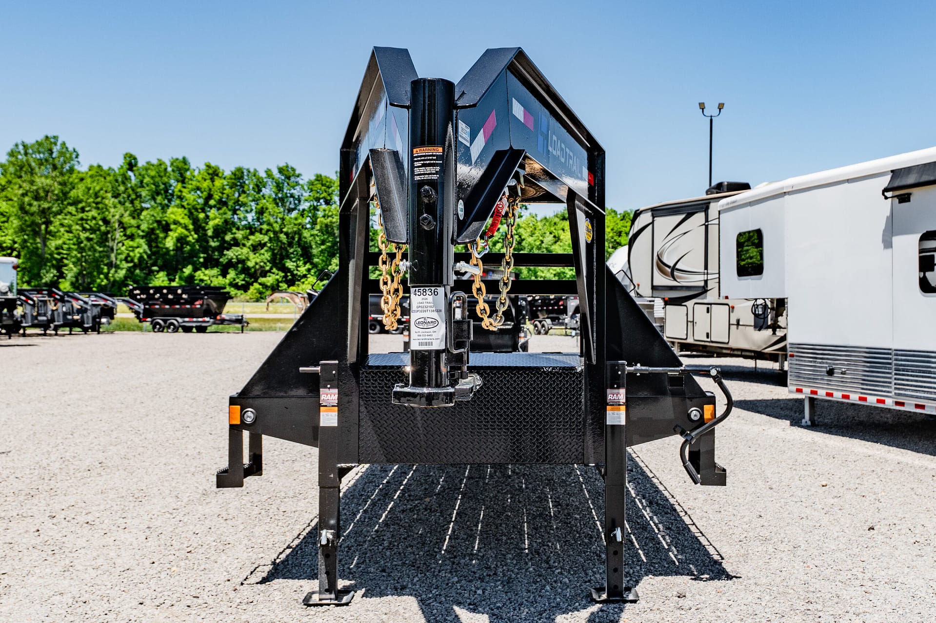 Close-up of a heavy-duty black trailer hitch with gold safety chains and warning labels on a gravel surface.