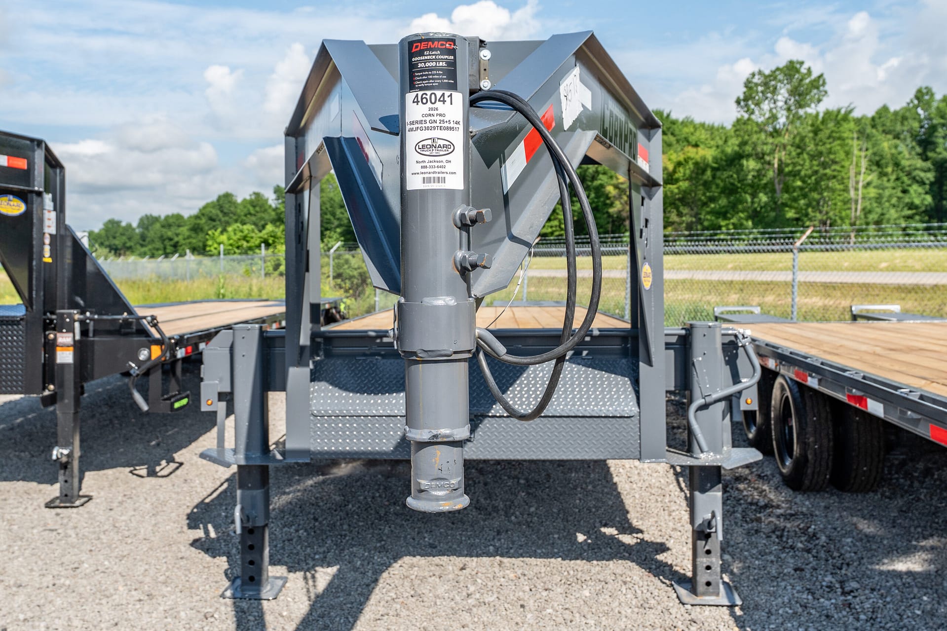 Close-up of a heavy-duty trailer hitch and hydraulic hoses on a gray industrial trailer in a gravel lot.