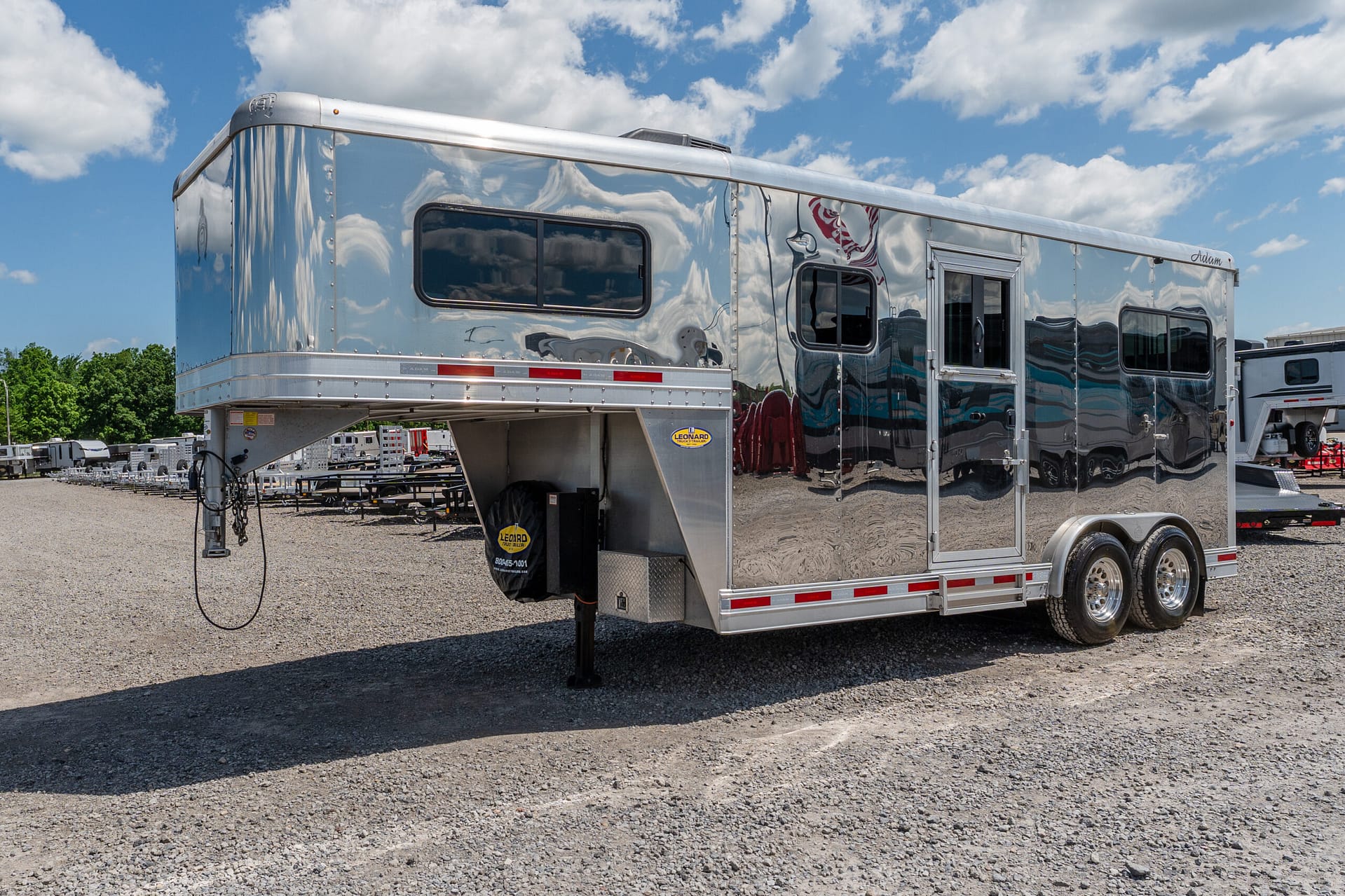 Shiny silver travel trailer parked on a gravel lot beneath a blue sky with clouds.