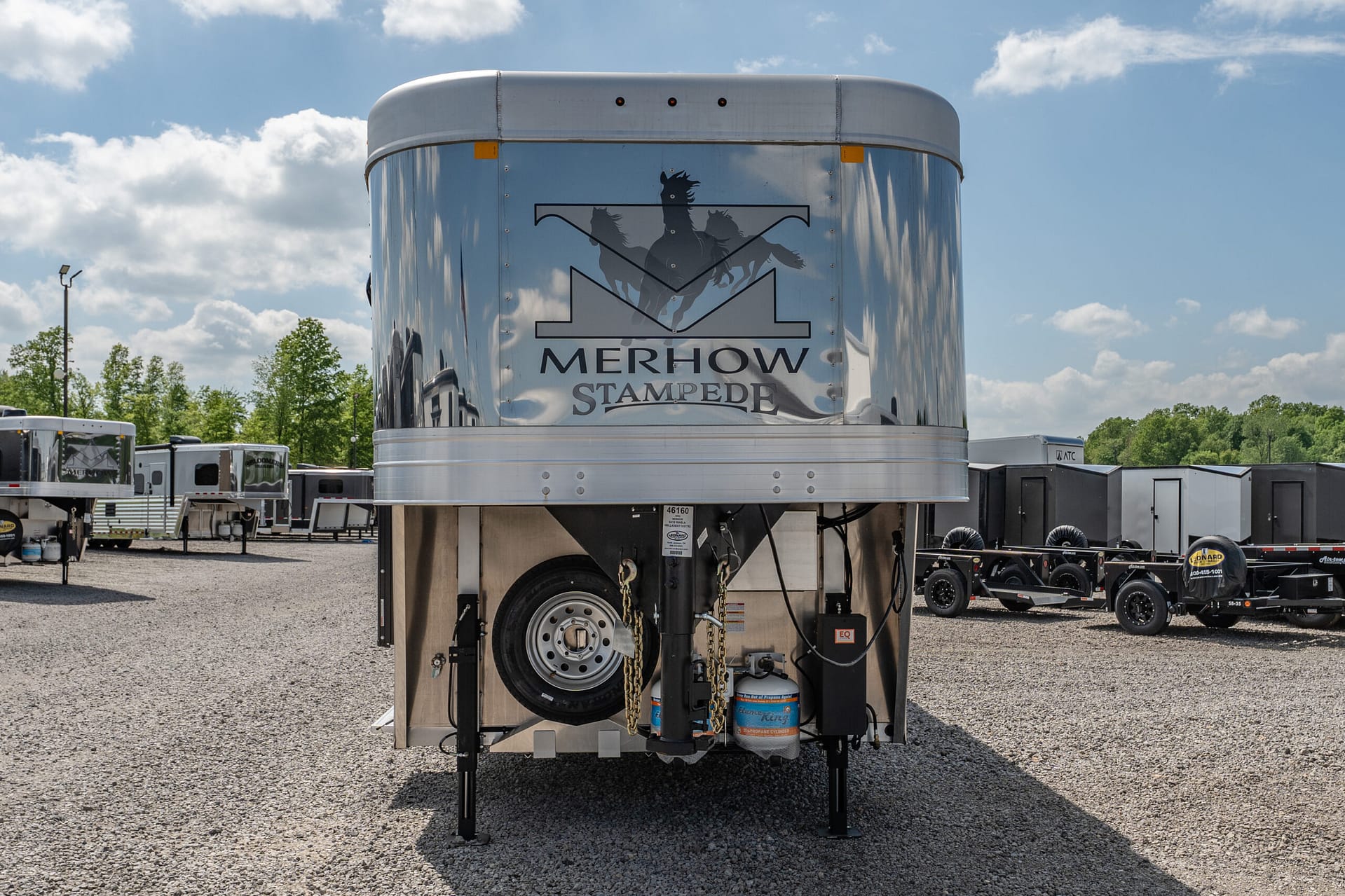 Front view of a silver Merhow Stampede horse trailer with logo, parked on a gravel lot.
