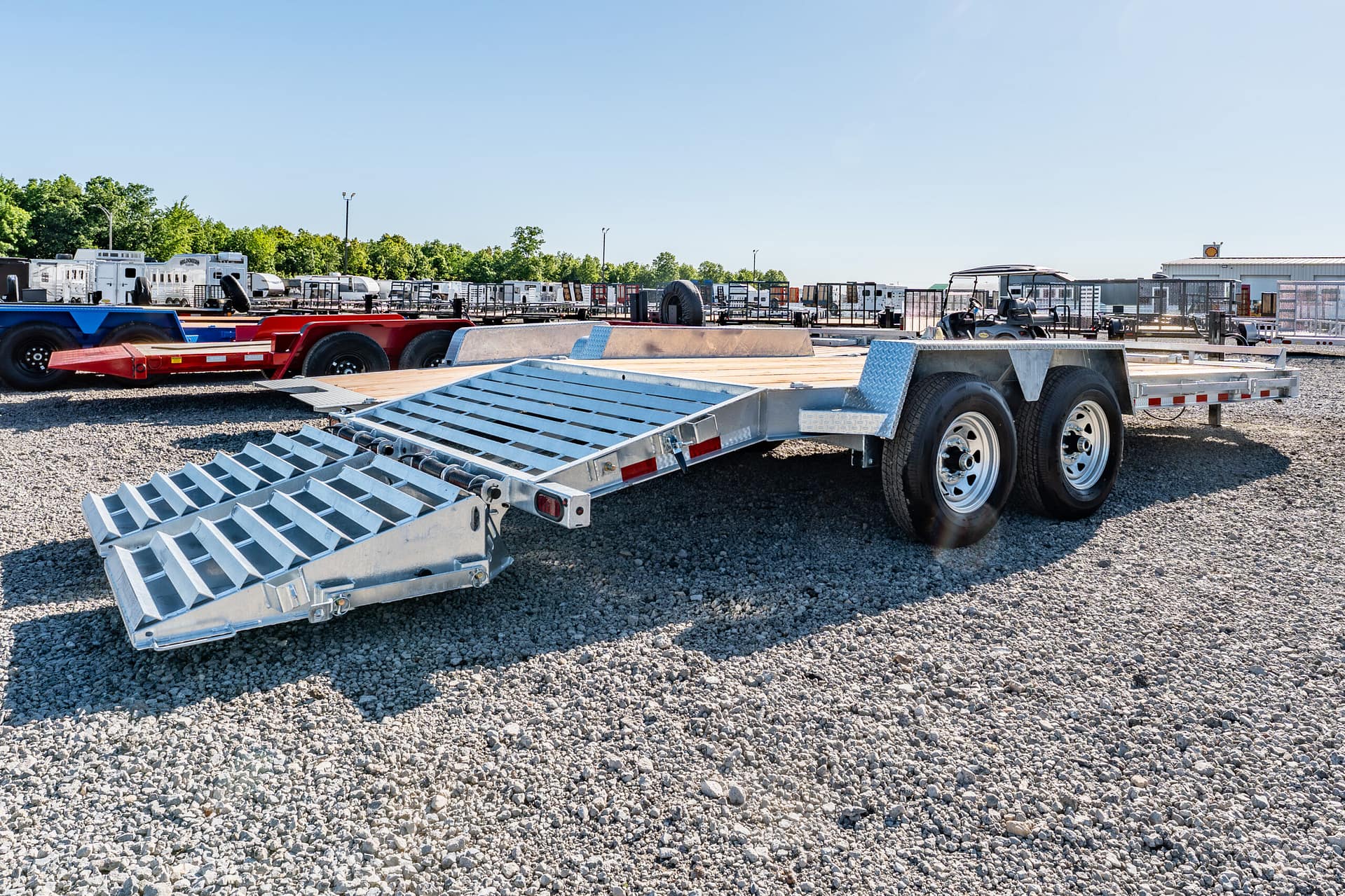 Metal flatbed trailers parked in a gravel lot under a clear blue sky.