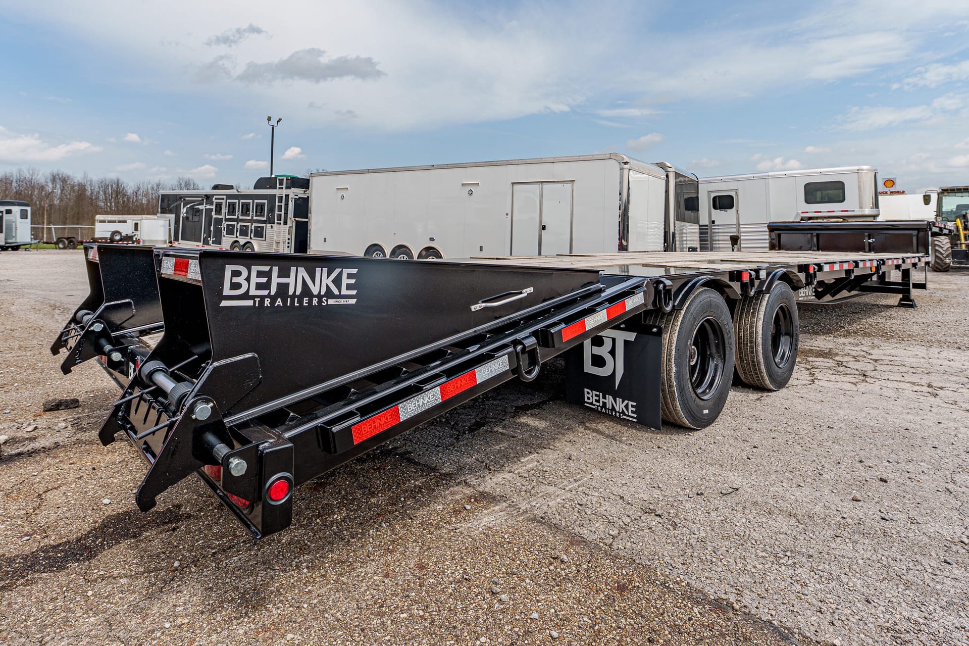 Black Behnke Trailers lowboy trailer with three axles on a gravel lot, other trailers in background