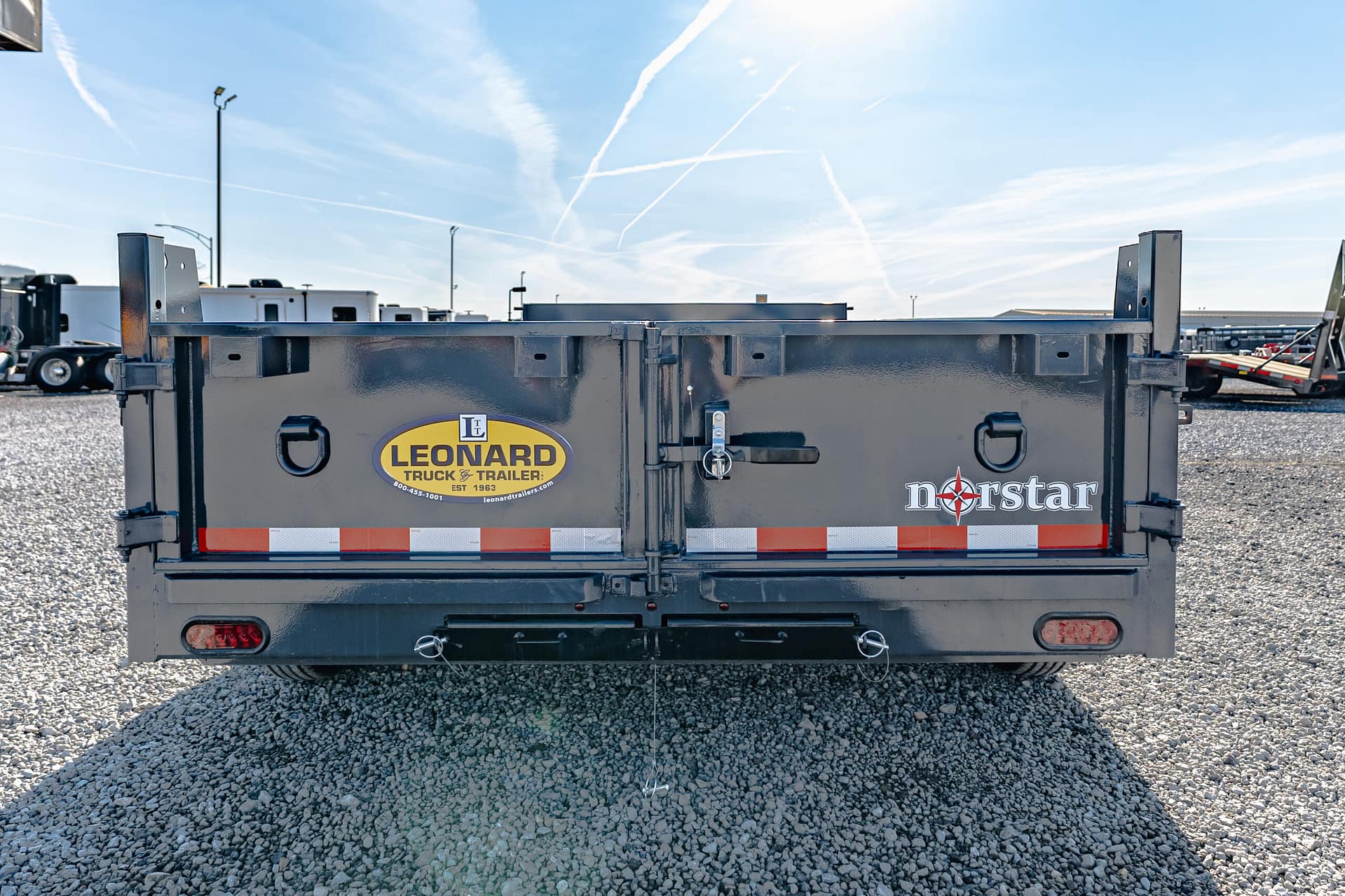 Rear view of a gray trailer with Leonard Truck & Trailer logo on the back, plus a Norstar logo, in a gravel trailer yard with other trailers in the background.