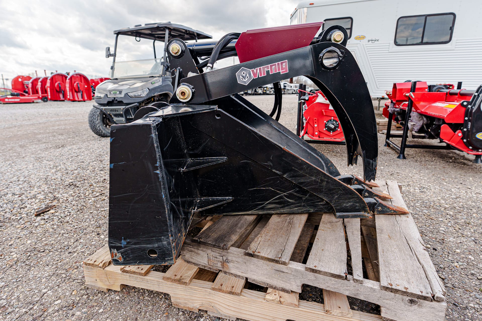 Black Viking bucket attachment resting on a wooden pallet in an outdoor equipment yard with red machinery in the background.