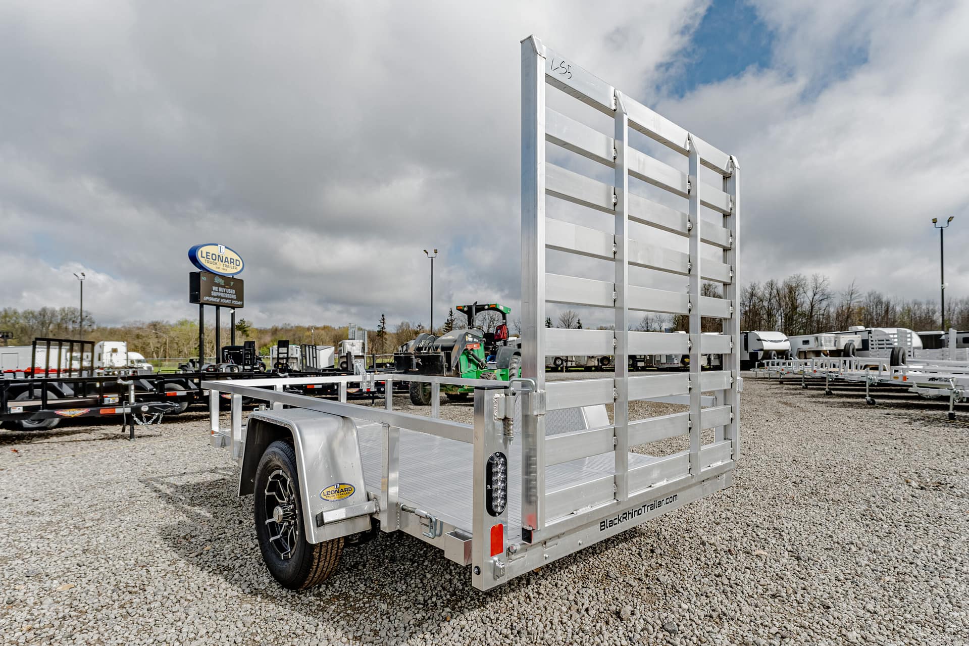 Aluminum utility trailer with tall side rails in a gravel lot at a trailer dealership.
