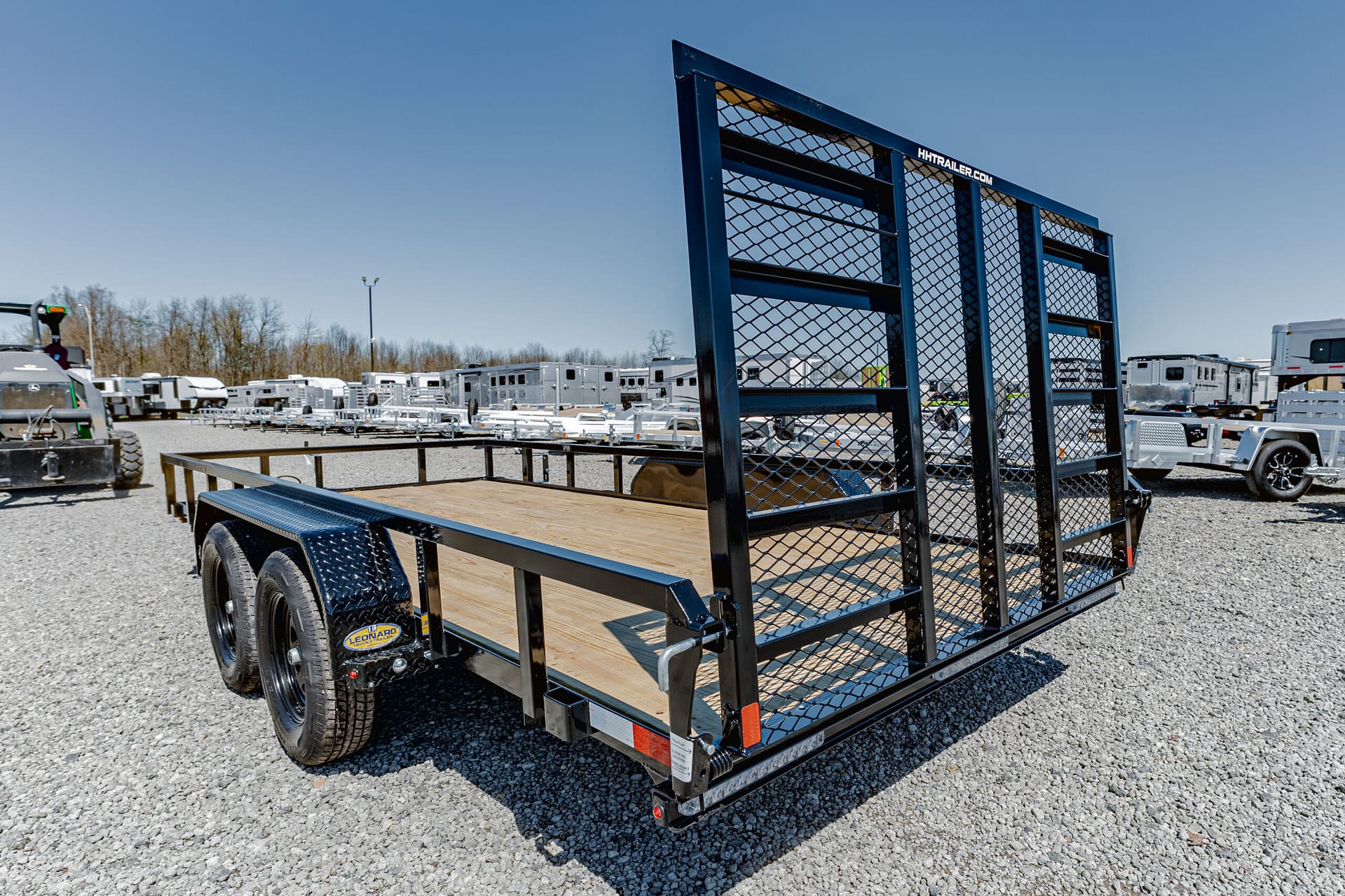 Flatbed utility trailer with a metal mesh ramp gate on a gravel trailer lot