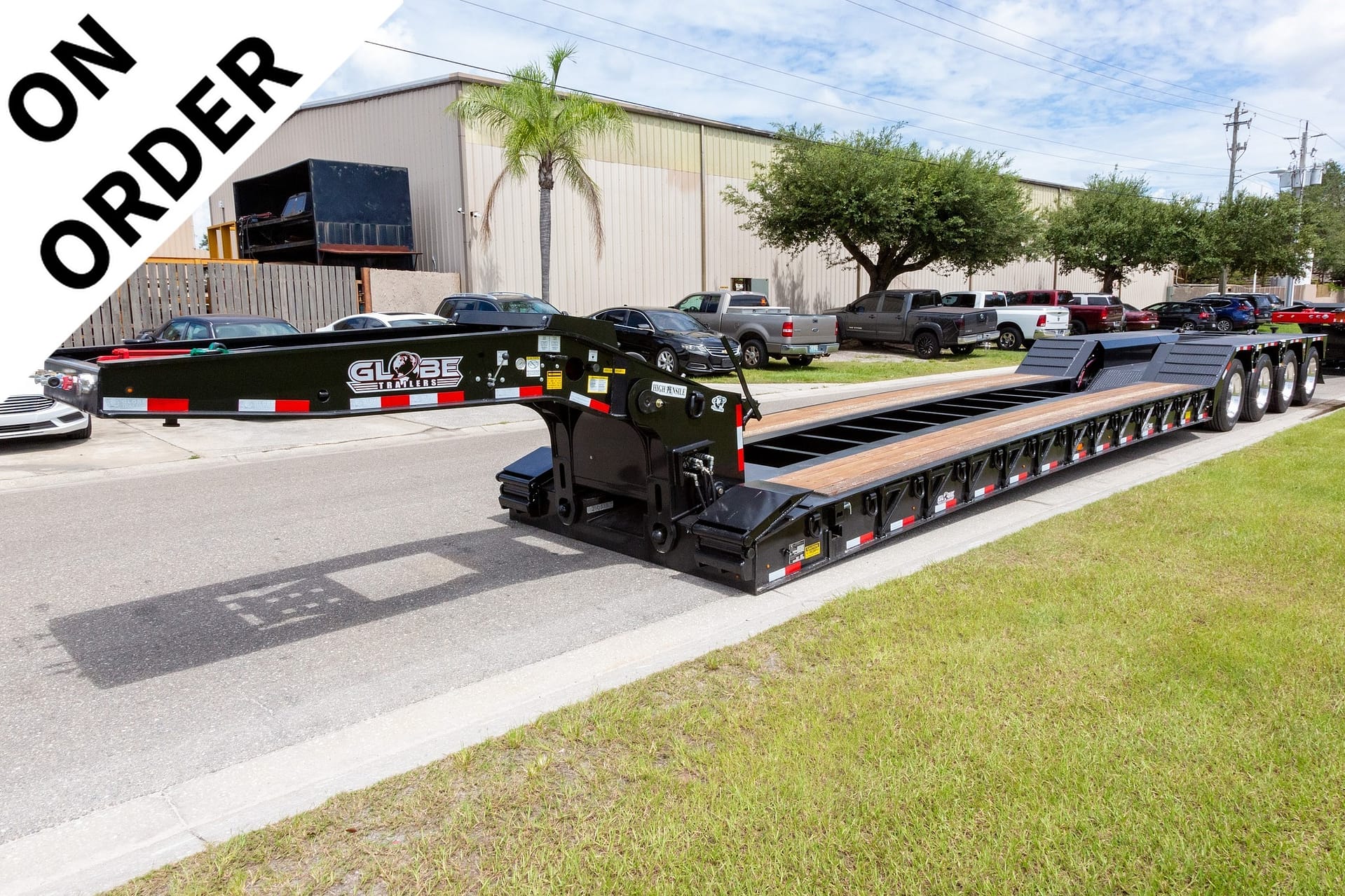 Long black flatbed trailer with Globe Trailers logo parked on a street beside a grassy curb, with a diagonal 'ON ORDER' banner in the top-left corner.