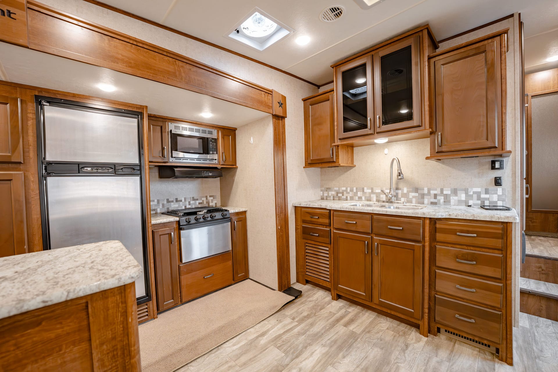RV kitchen with stainless steel fridge, stove, microwave, and brown wooden cabinets.