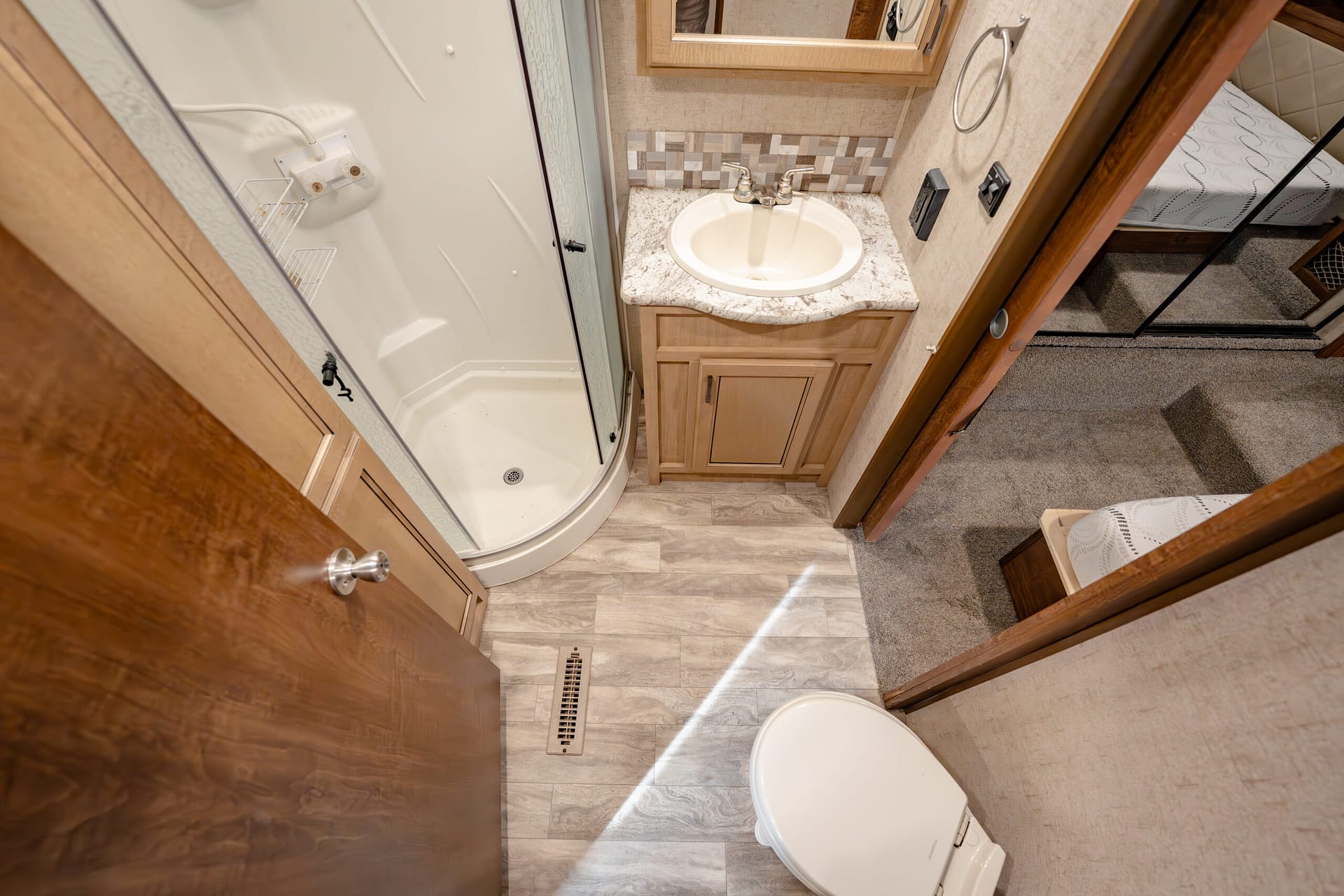 Compact RV bathroom with curved shower, sink vanity, and toilet; wood cabinets and beige tones.