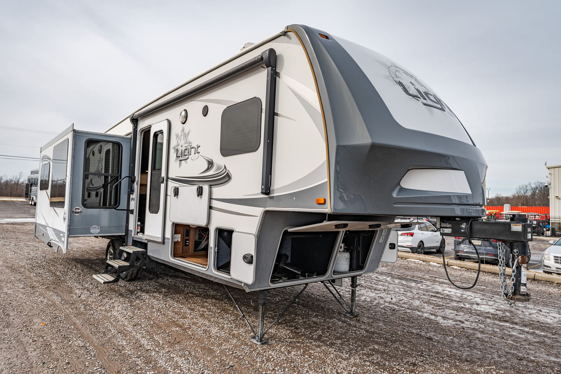 Large fifth-wheel RV with a side slide-out and open entry door on a gravel lot, ready for camping use by a campground.