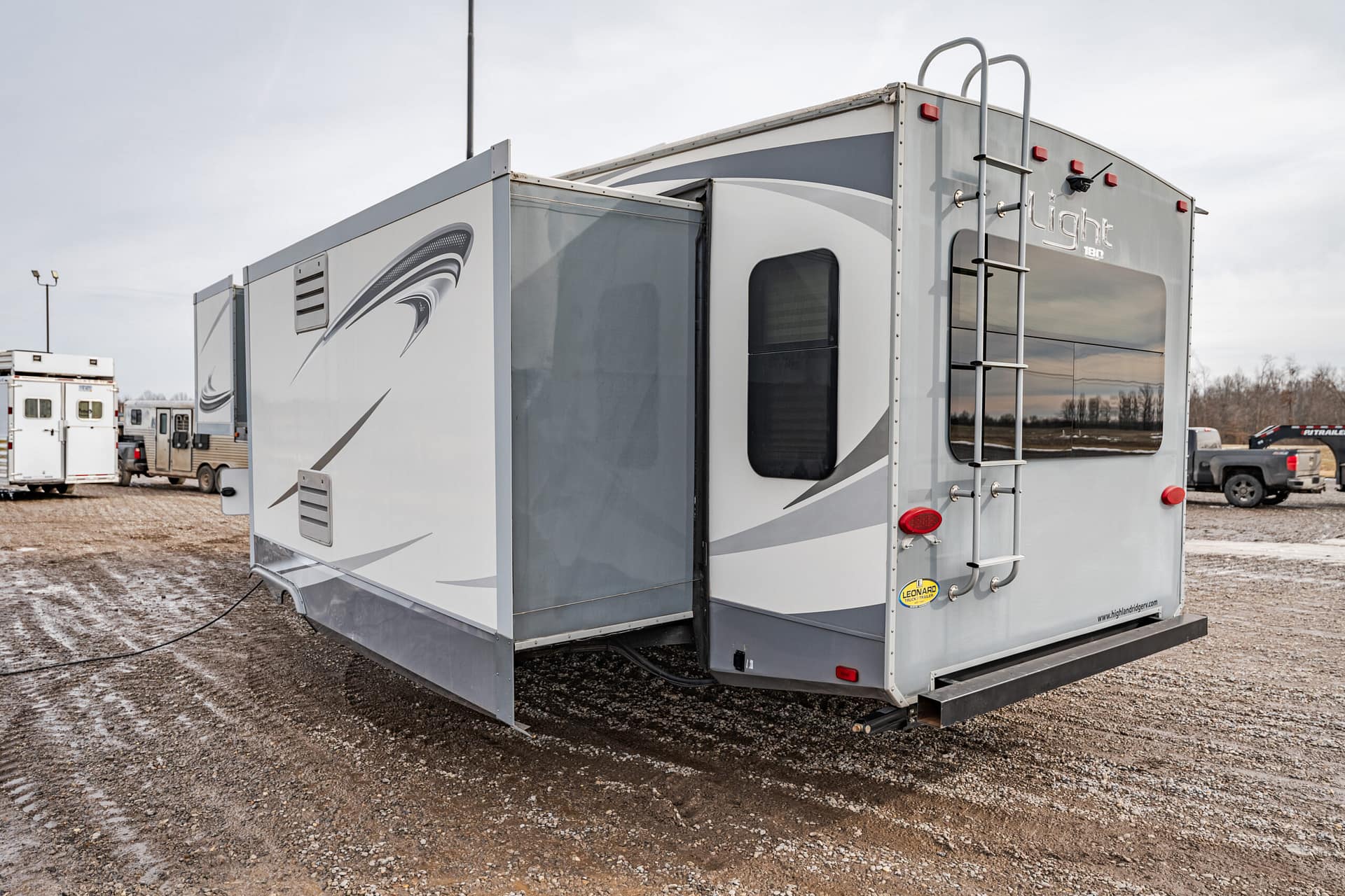 Travel trailer with a side slide-out extended, parked on a gravel lot.