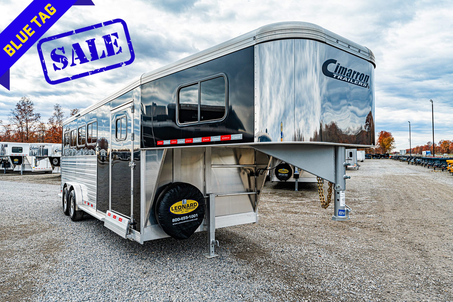 Shiny silver Cimarron gooseneck trailer on a gravel lot for sale with a prominent blue SALE banner in the corner.