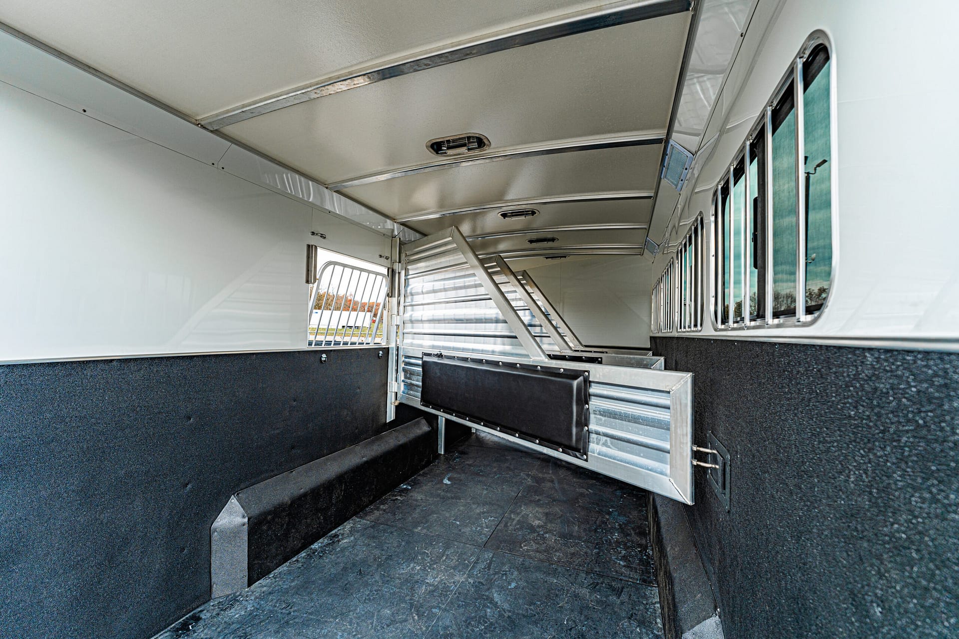 Interior of a horse trailer with metal partitions and black padded stalls along the sides, ready for loading horses
