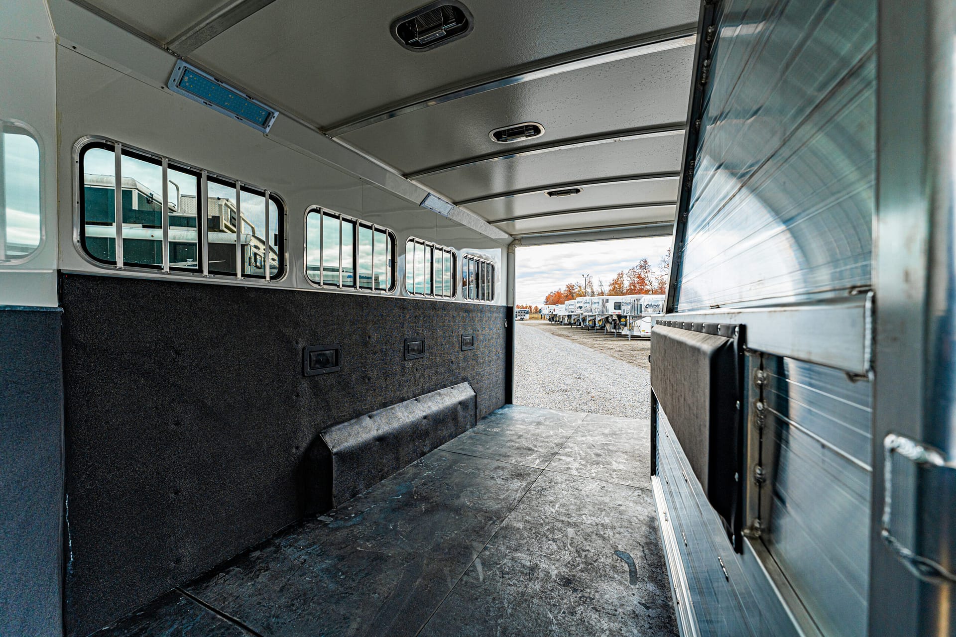 Interior of an empty horse trailer with a row of side windows and a textured rubber floor.
