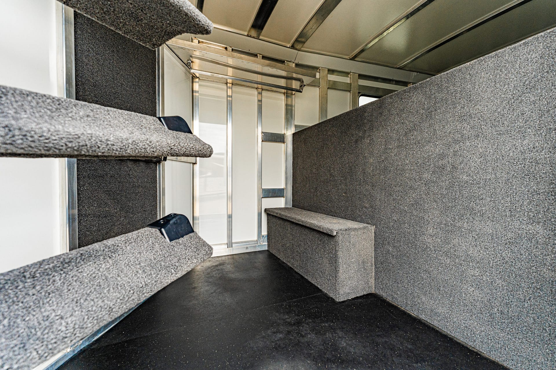 Interior of a gray-carpeted trailer with angled steps on the left and a padded divider bench along the right wall.
