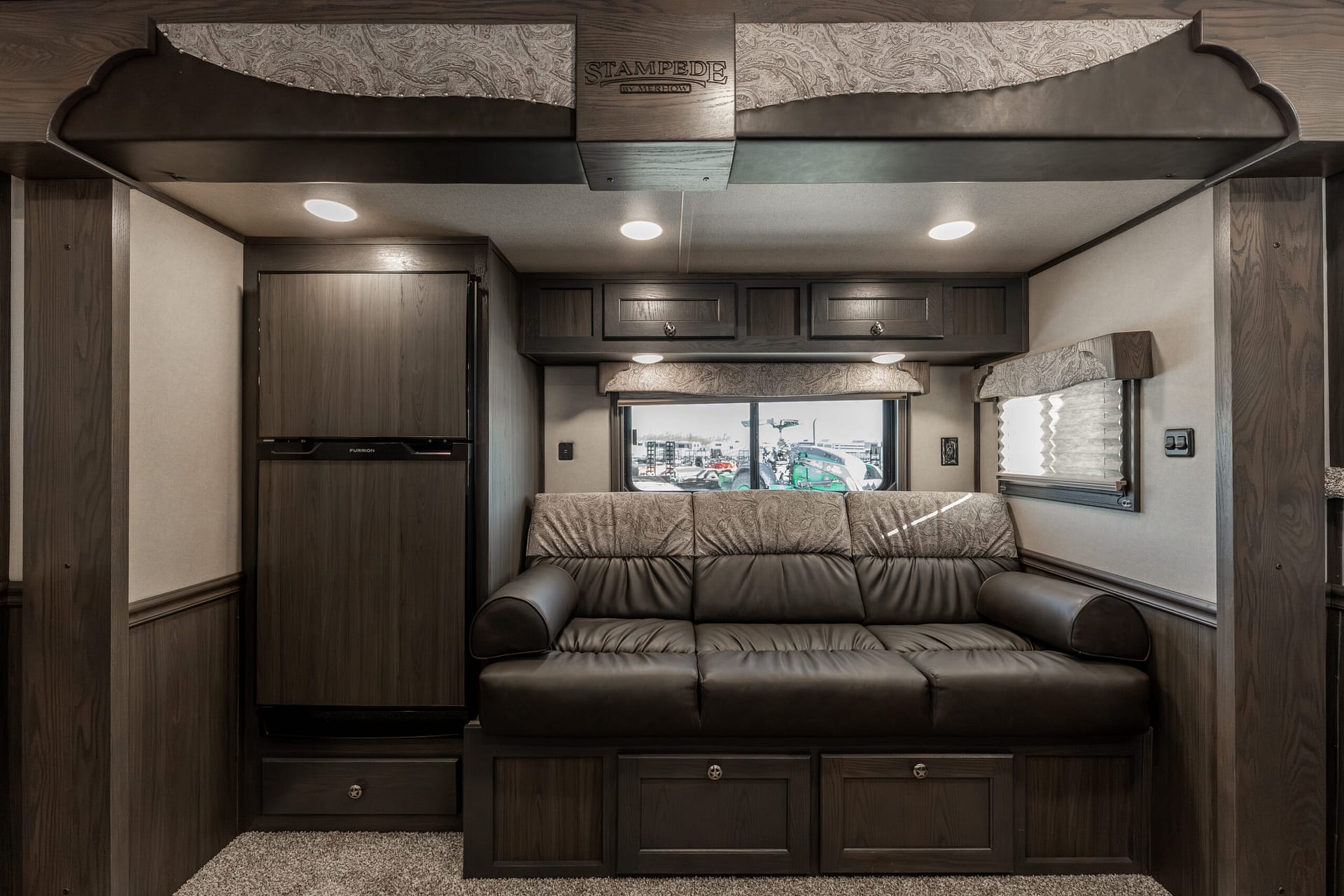 Cozy RV living area with dark wood cabinets, a leather sofa, and overhead storage cabinets.