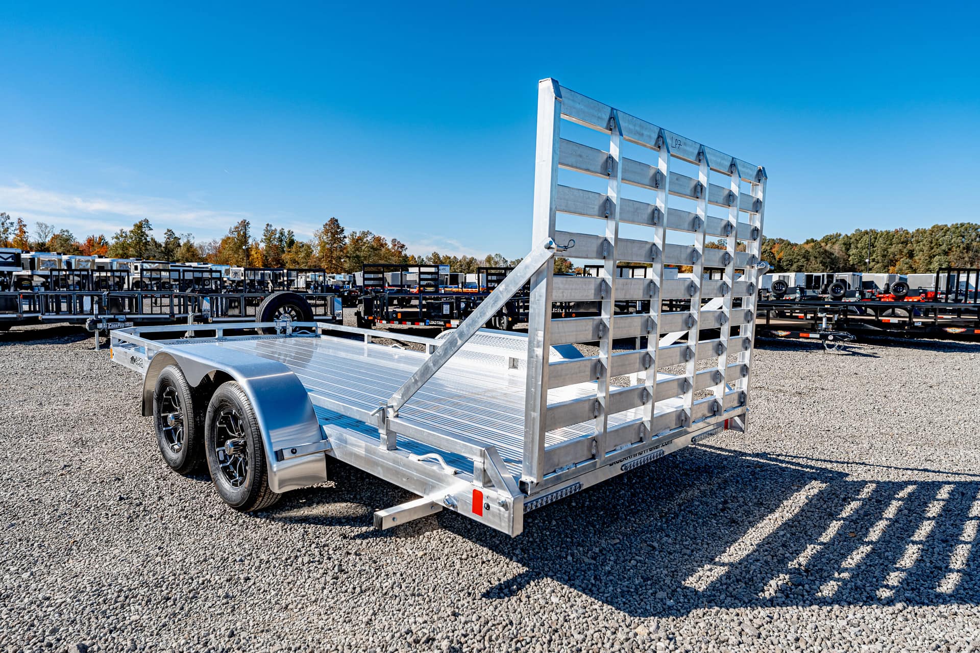 Aluminum tandem-axle flatbed trailer with a raised rear gate on a gravel lot