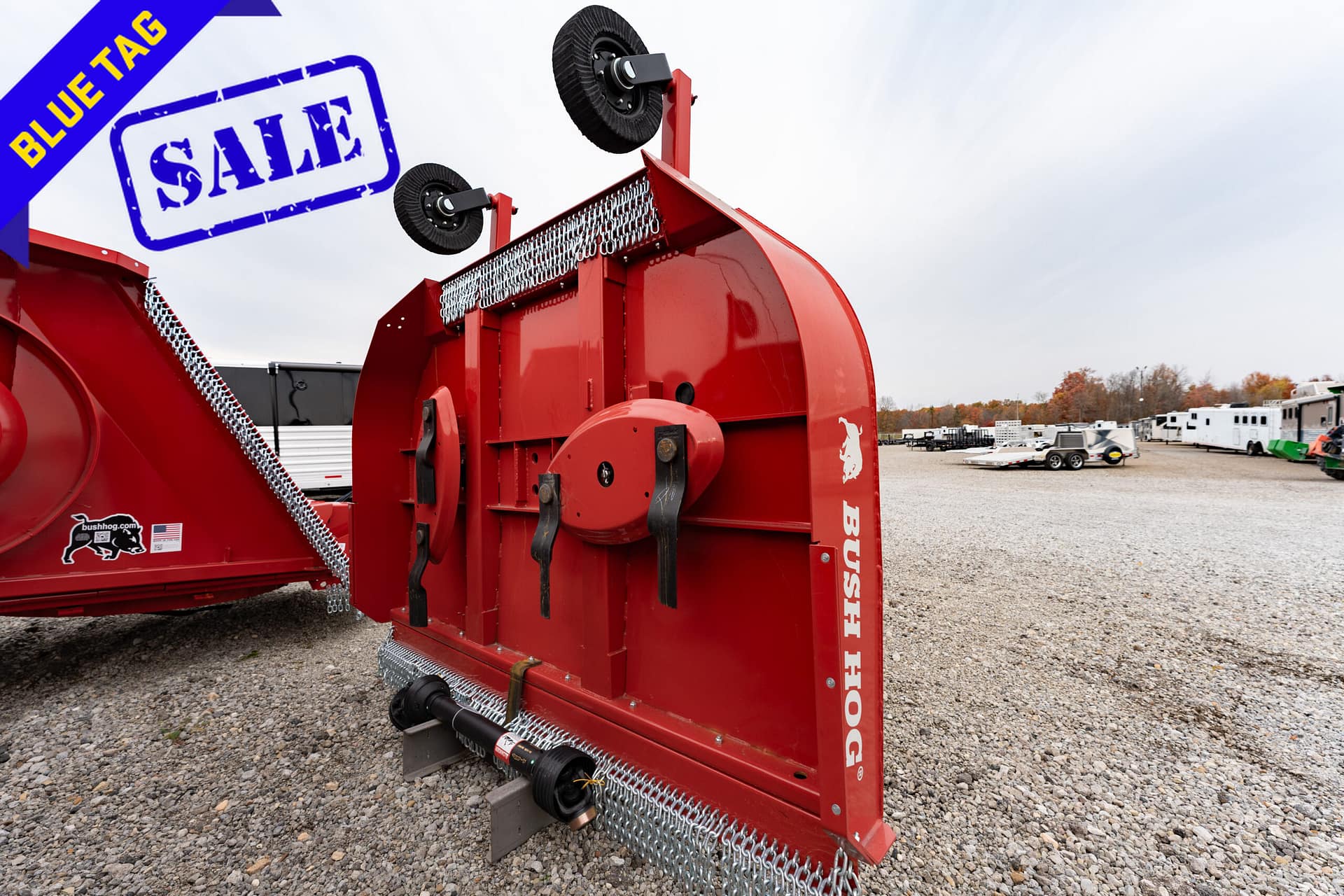 Large red Bush Hog agricultural implement on a gravel lot, with a blue 'Blue Tag Sale' banner in the corner.