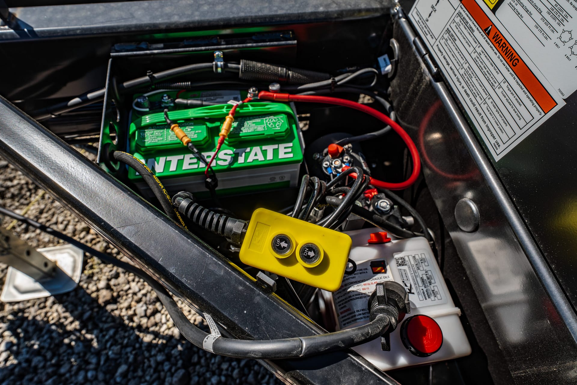 Close-up of a green Interstate battery with red and black cables and assorted wires in a vehicle’s engine bay.