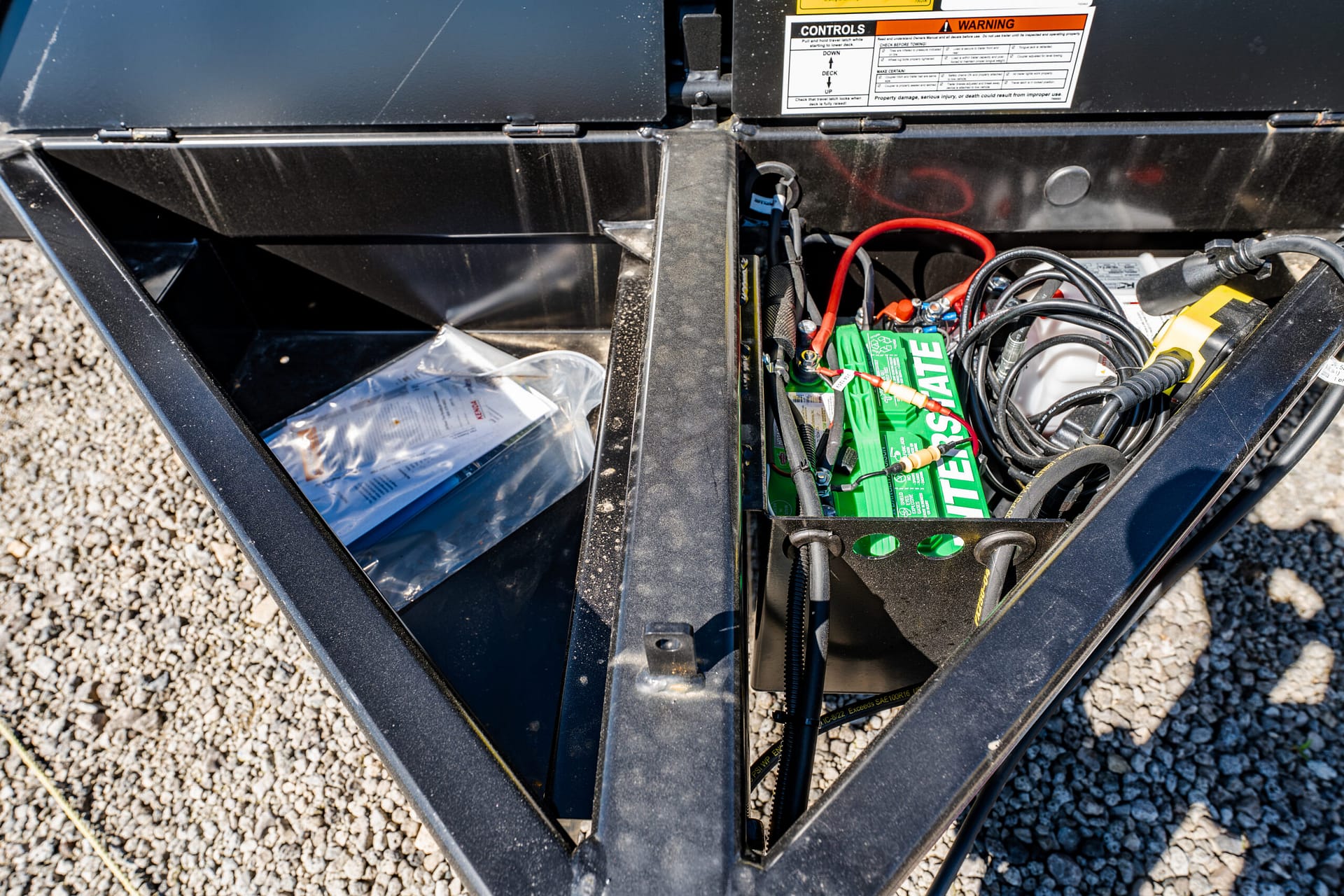 Open battery compartment with tangled red and black cables, a green battery, and a warning label on a metal box.