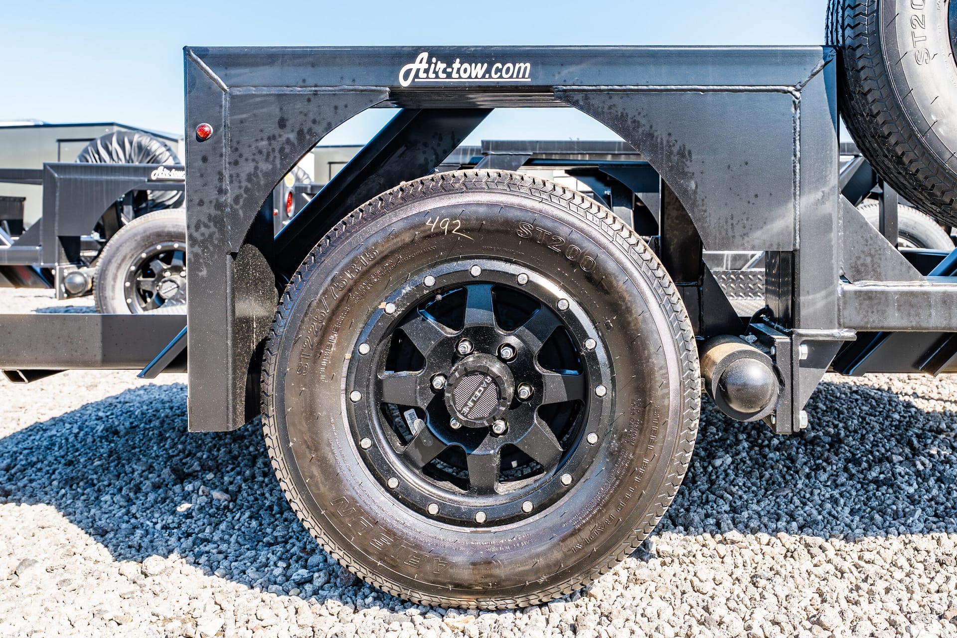Close-up of a black trailer wheel and spare mounted on a gray metal frame, with 'Air-tow.com' branding visible on top edge.