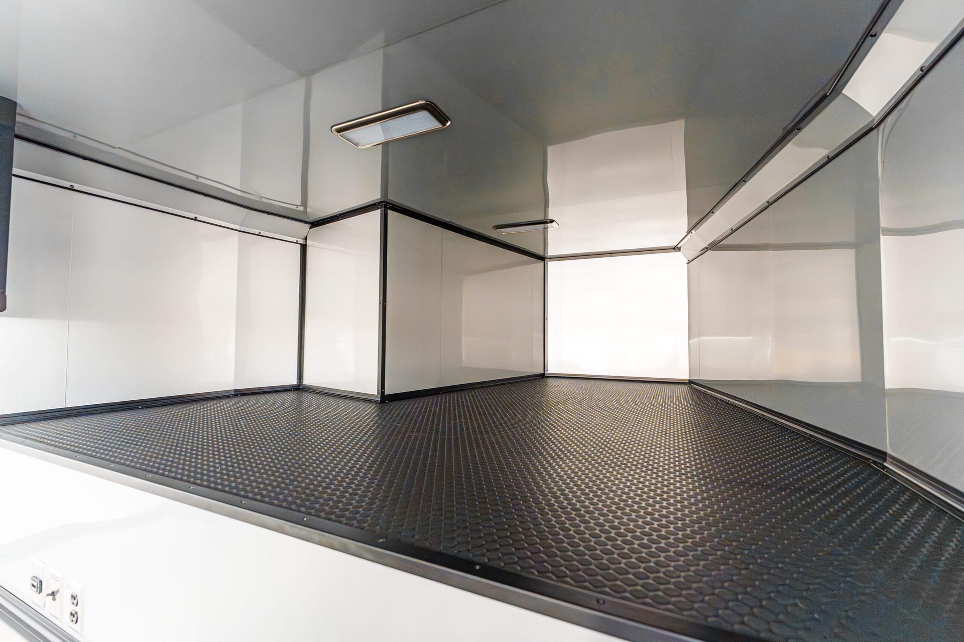 Empty industrial interior with steel-gray walls and a diamond-plate floor, bright overhead lights present in the space.