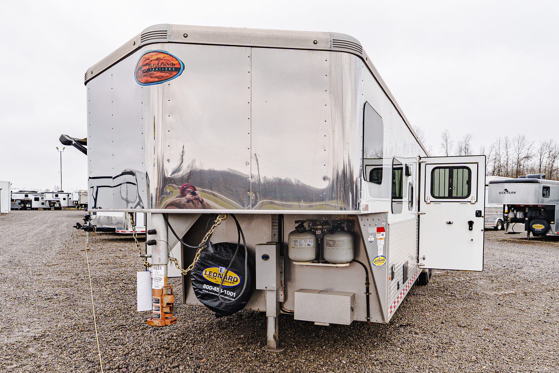 Shiny aluminum semi-trailer in a gravel lot with a Leonard Truck & Trailer logo on the back panel in view.