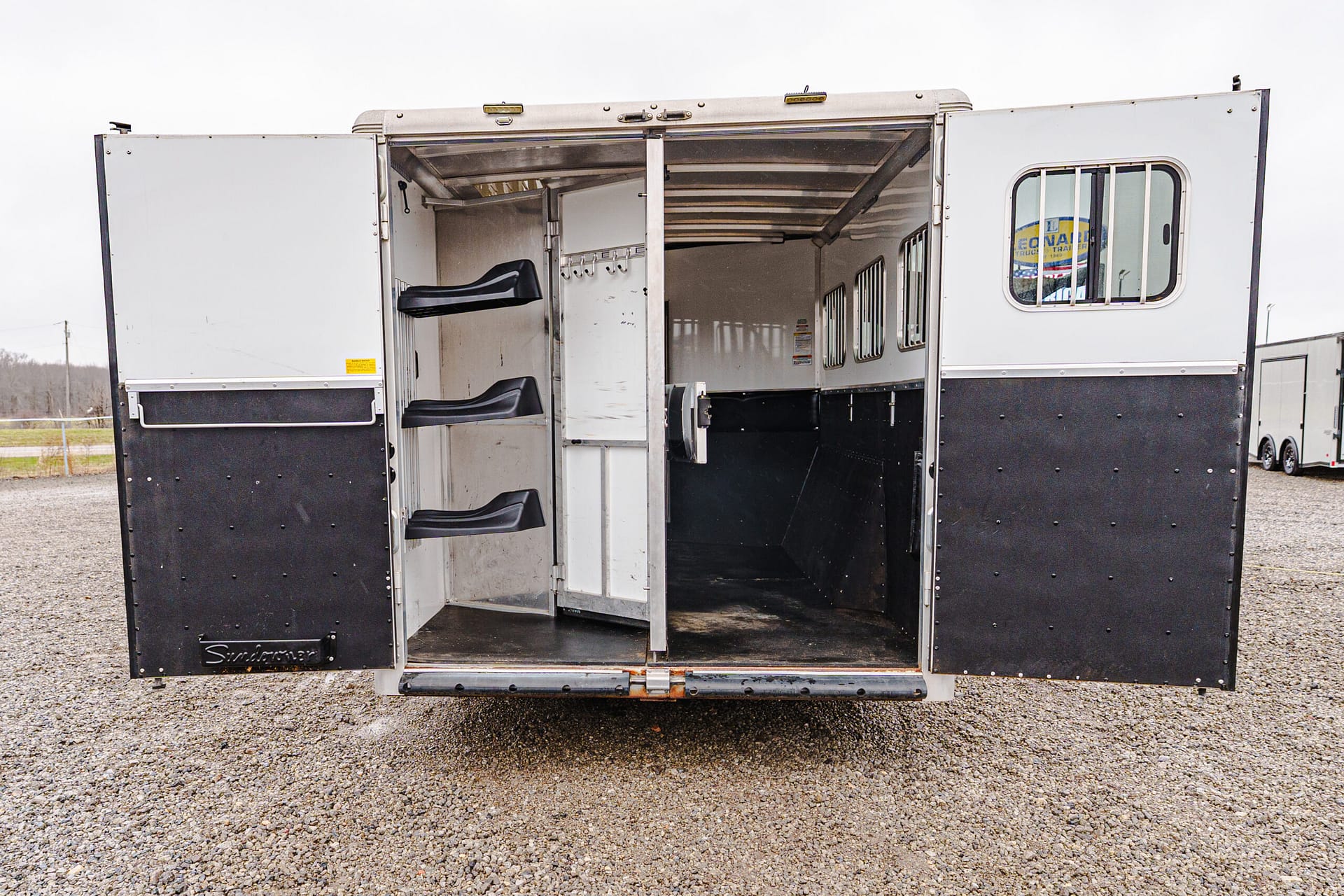 Interior of an open horse trailer with two-tier black seats along the left wall and hanging hooks on the partition.