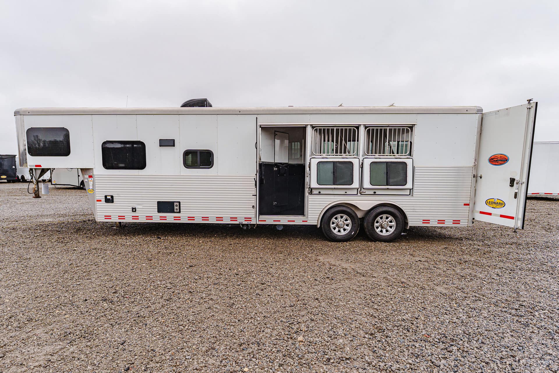 White travel trailer with multiple windows and a slide-out, parked on a gravel lot under an overcast sky