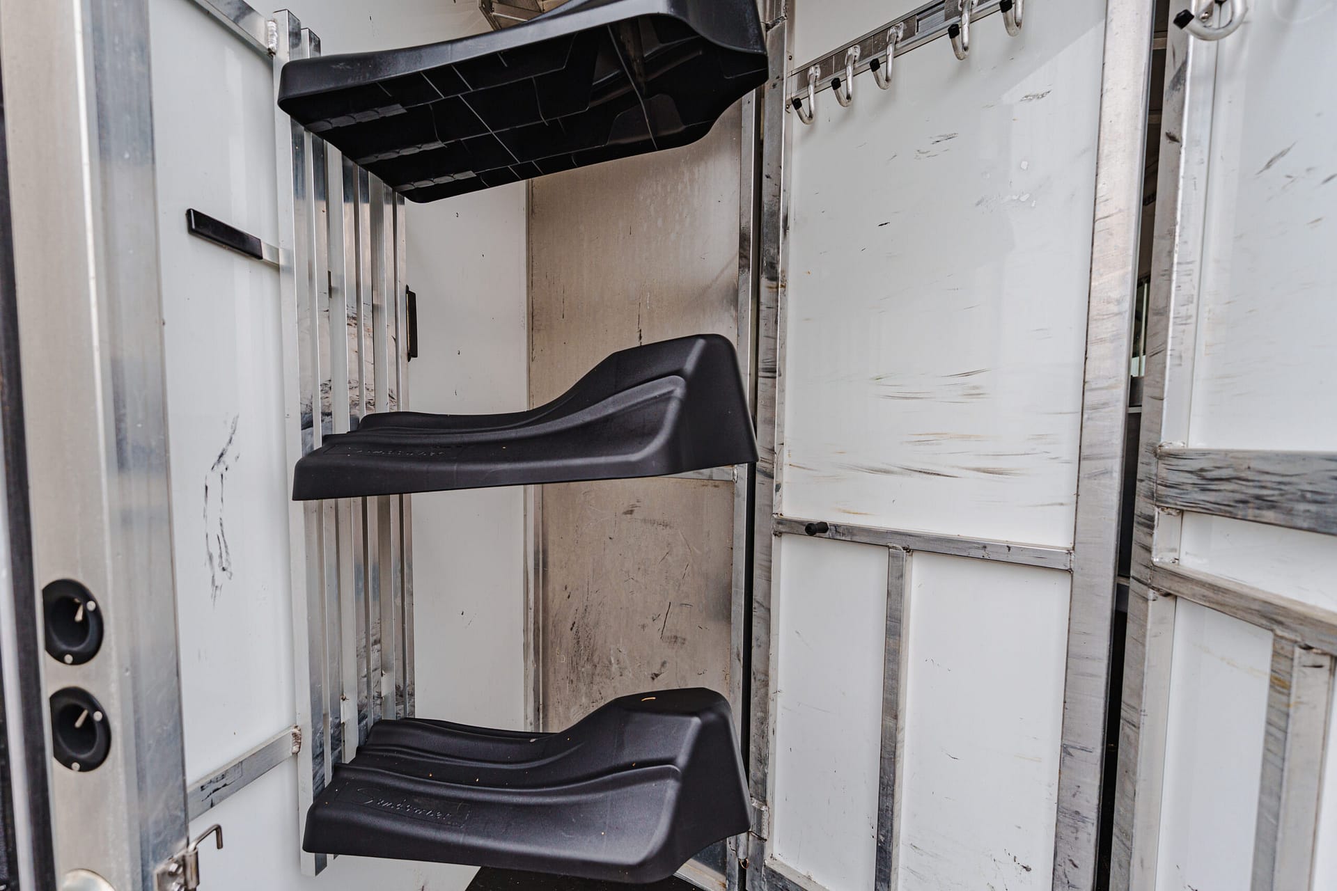 Interior of a metal industrial cabinet or elevator with black molded seats attached to the walls, showing wear and scratches.