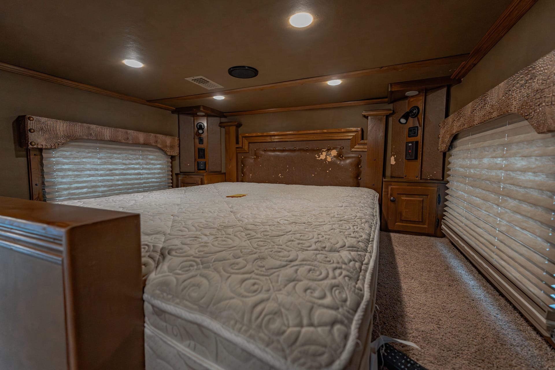 Interior of a coach RV bedroom with a large quilted bed, wood headboard, and built-in cabinets along both walls
