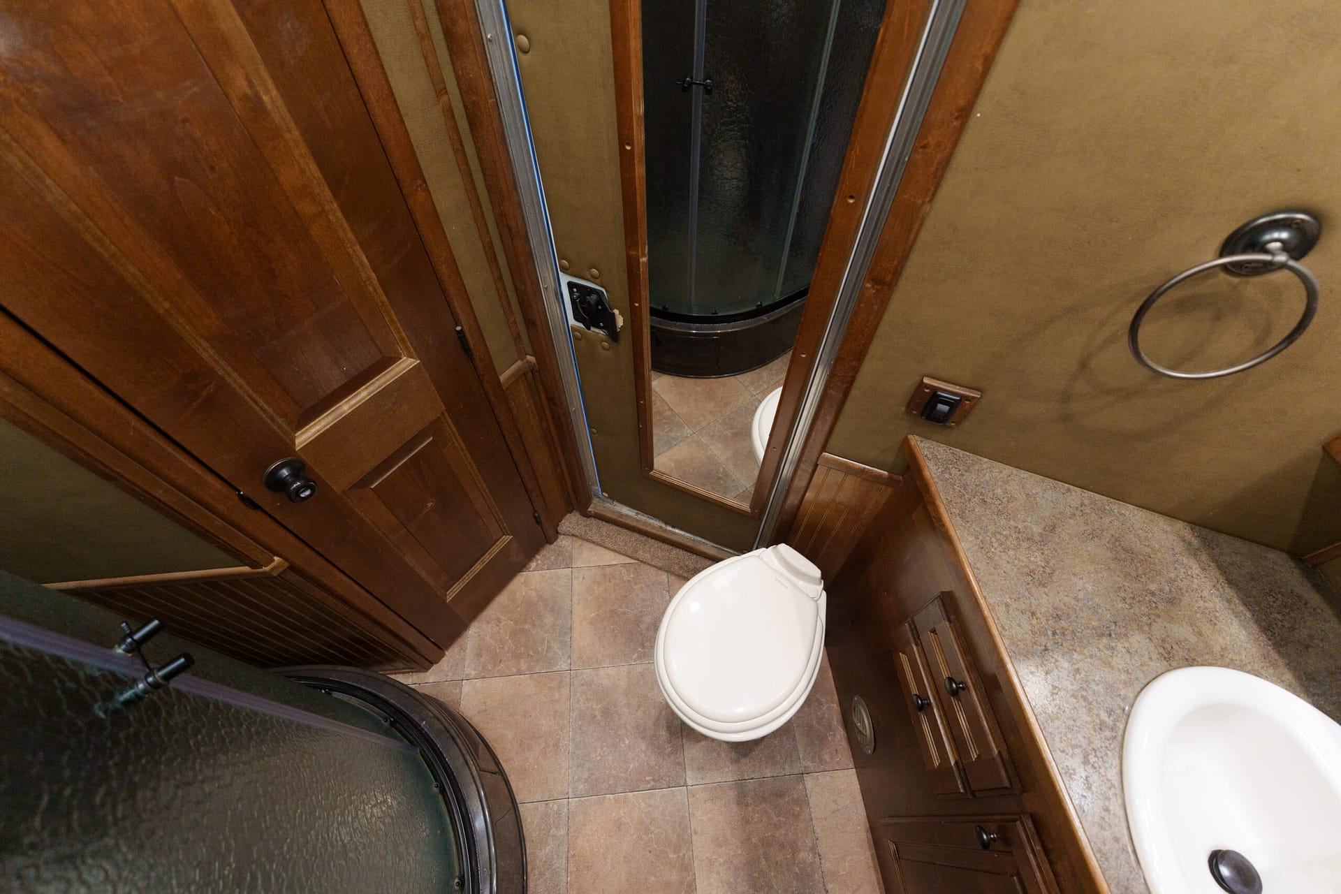 Compact RV bathroom with dark wood cabinets, tile floor, and a curved shower stall next to a toilet.