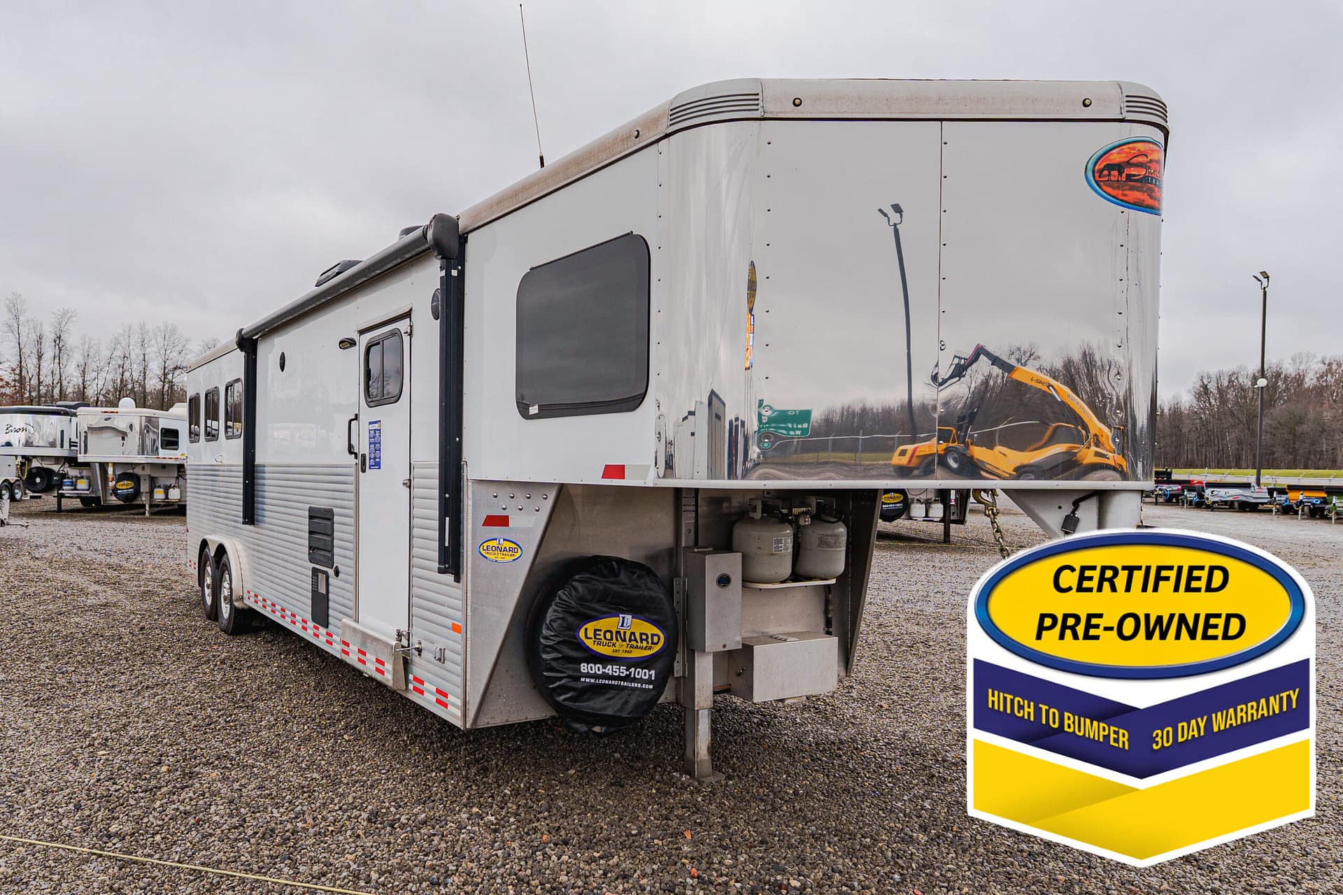 Large silver semi-trailer with a curved front, parked on a gravel lot beside a bright yellow 'Certified Pre-Owned' sign in the foreground.
