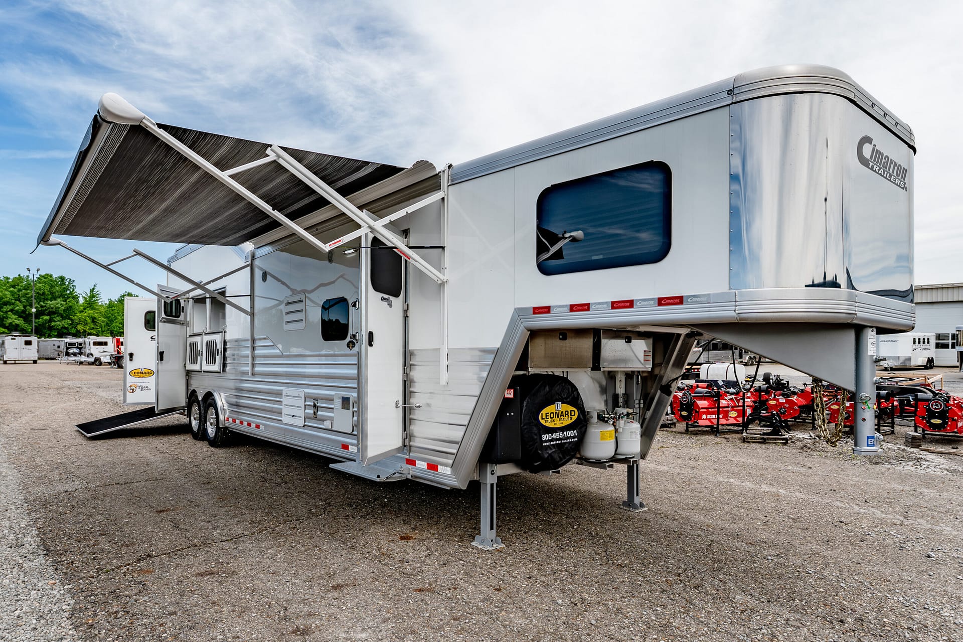 White travel trailer with a large retractable awning extended in a gravel lot, Cimarron Trailers visible on the side edge.