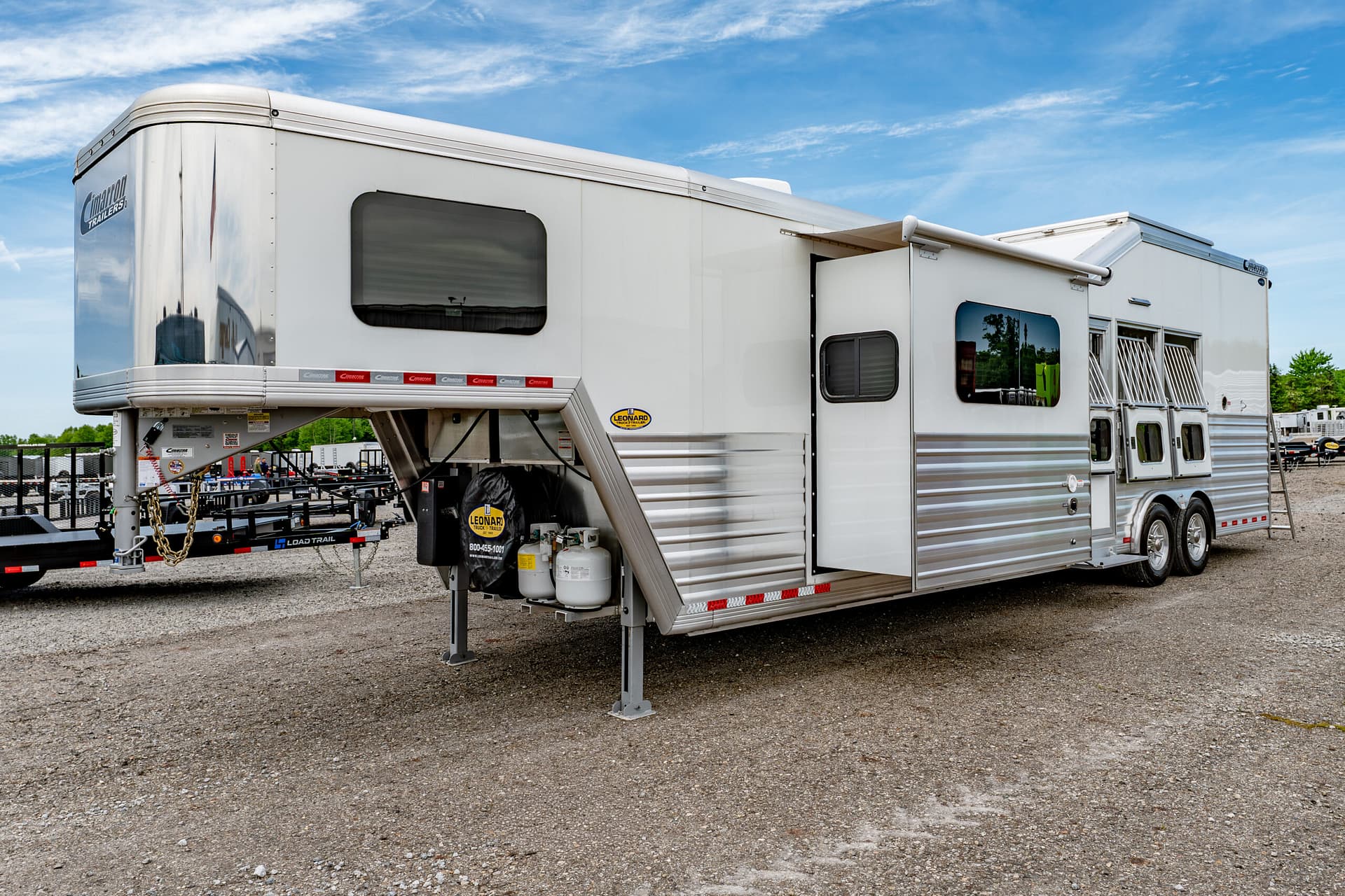 White fifth-wheel trailer with a side slide-out on a gravel lot against a blue sky.