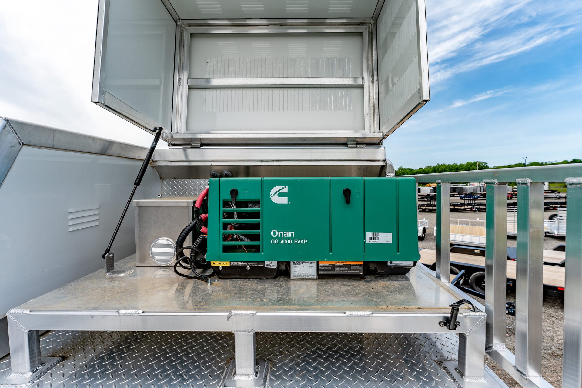 Green Cummins Onan QG 4000 EVAP generator mounted on a diamond-plate metal platform inside a stainless enclosure, outdoors under a blue sky.