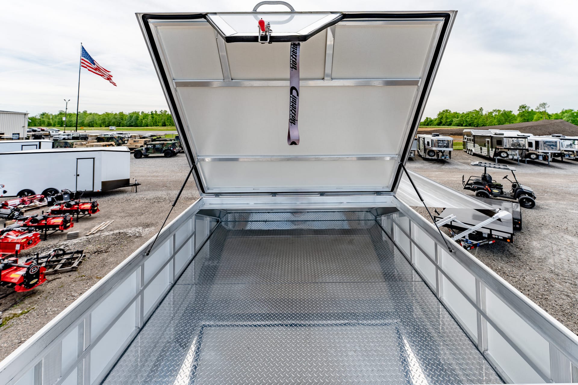 View from inside an open aluminum trailer bed looking out over a lot of trailers and equipment, with an American flag in the background.