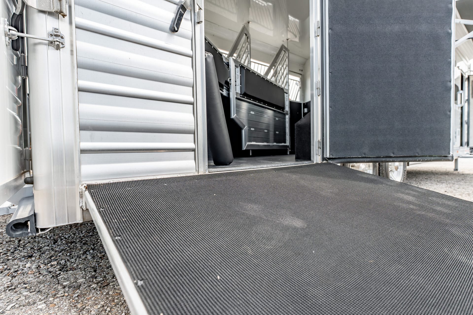 Loading ramp extended from a silver trailer showing a black textured ramp surface and interior equipment steps inside the trailer hallway.
