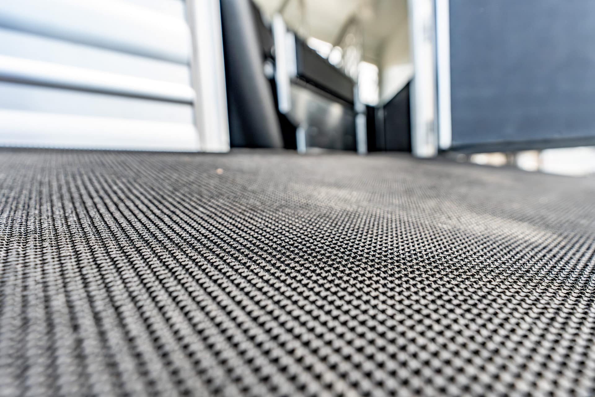 Close-up of a metal mesh floor with industrial walls forming a narrow corridor in the background, low-angle view.