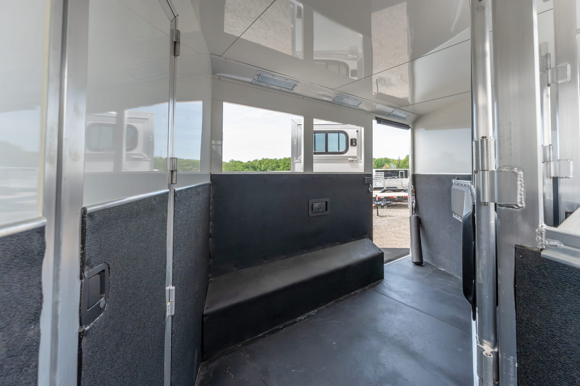 Interior of a silver livestock/horse trailer with black lower walls, a raised step platform, and daylight visible outside.