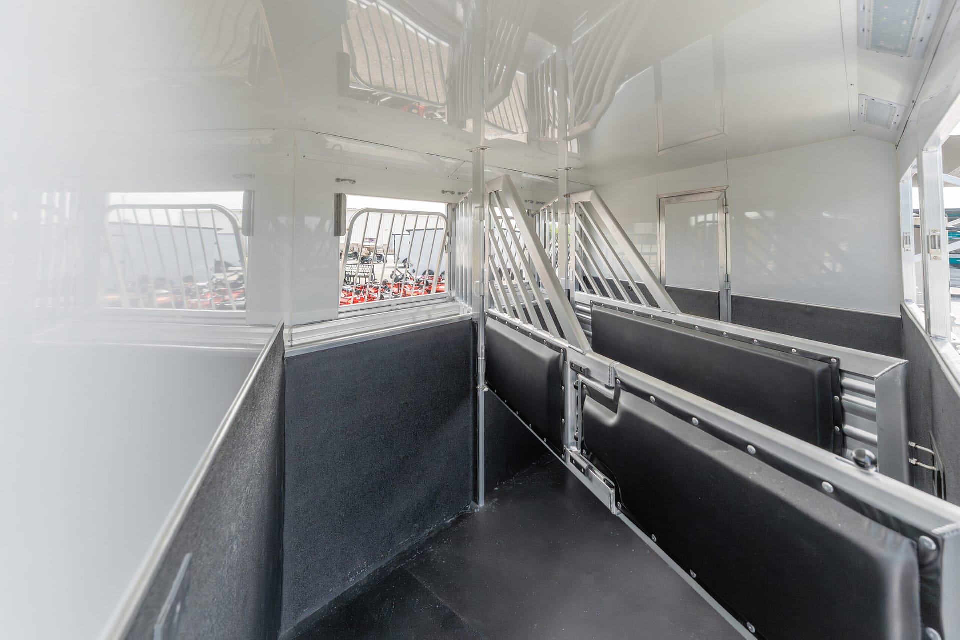 Interior of a white trailer with metal stall dividers and black floor padding, empty and ready for livestock or equipment transport.