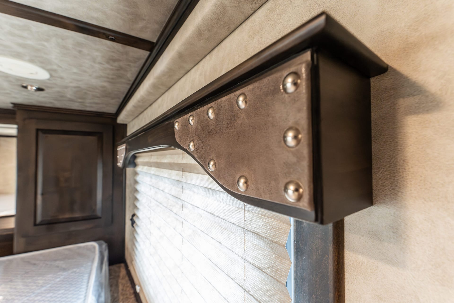 Close-up of a riveted metal panel above a window in an RV interior, with a fabric shade pulled down