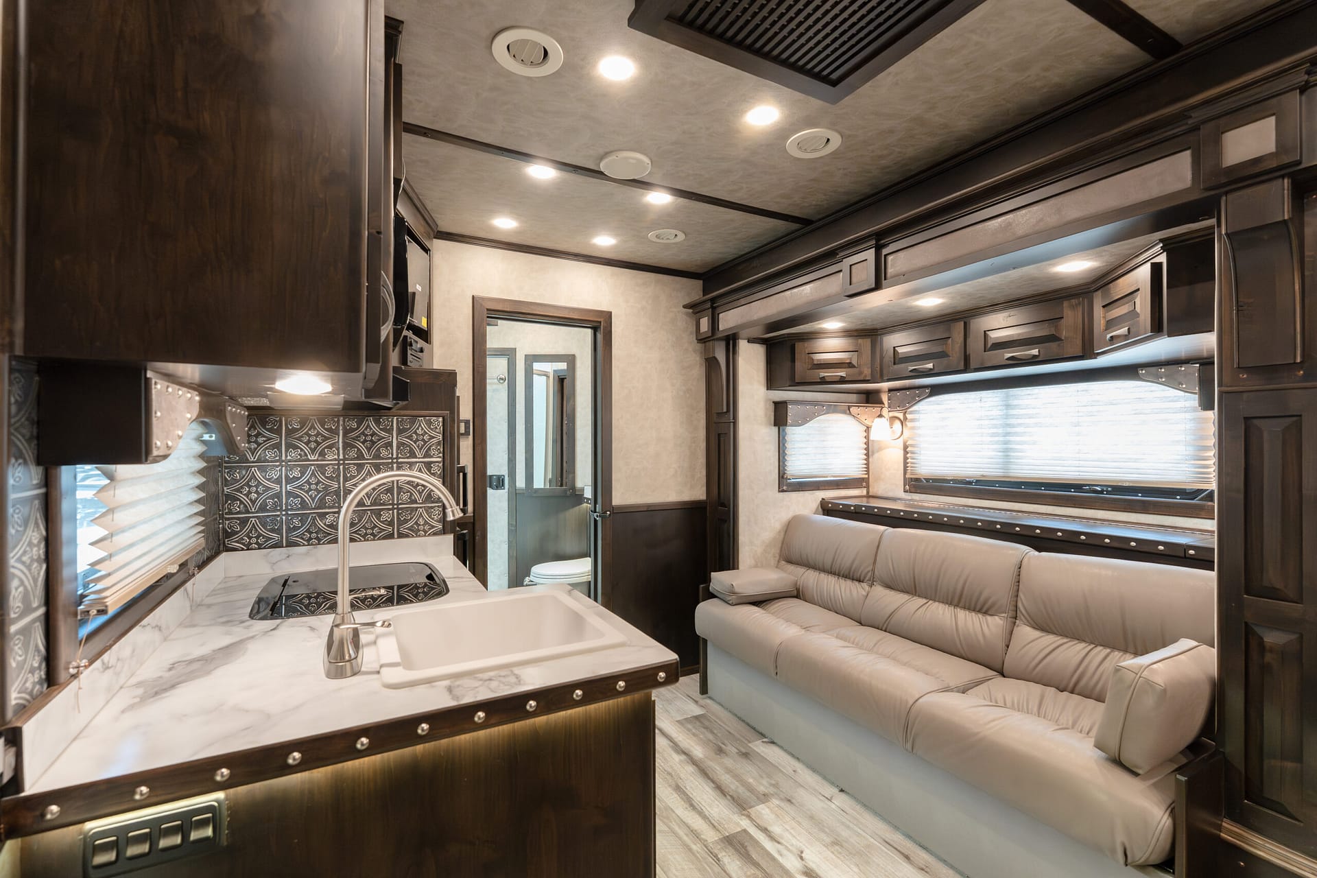 Interior of a modern RV with dark wood cabinets, marble countertop, and a stainless sink in a small kitchen area.