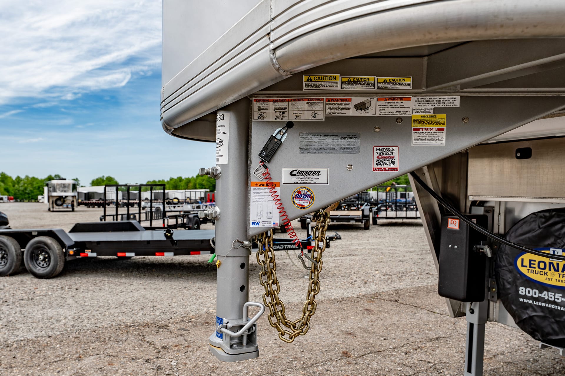 Close-up of a truck trailer hitch with safety chains and warning labels on the hitch area in a gravel lot